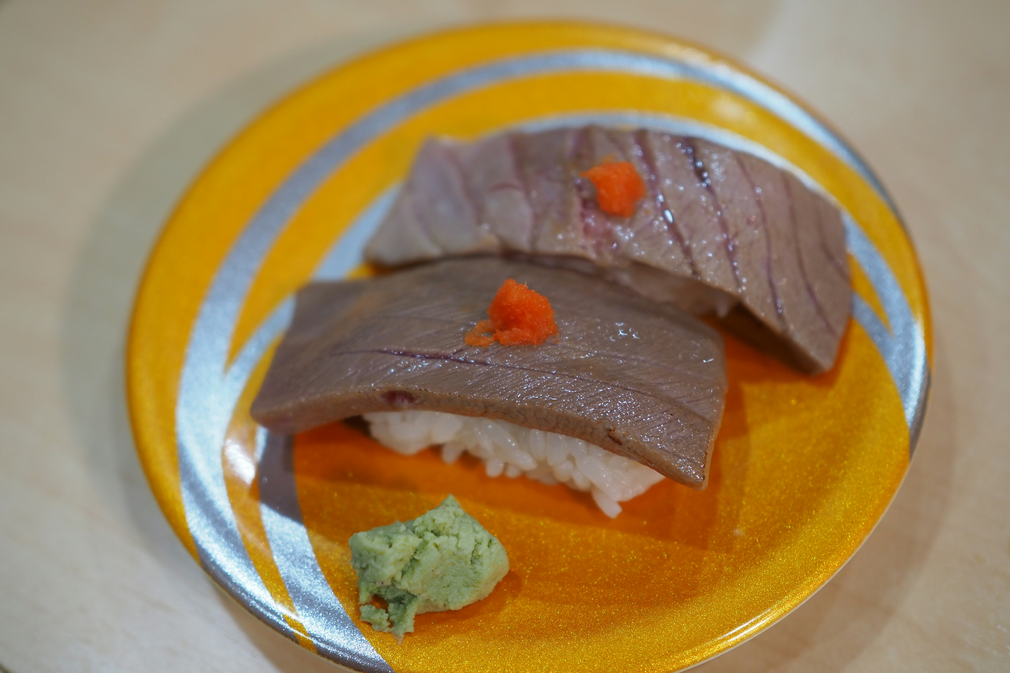 Sushi tuna diiris di atas piring oranye dengan wasabi