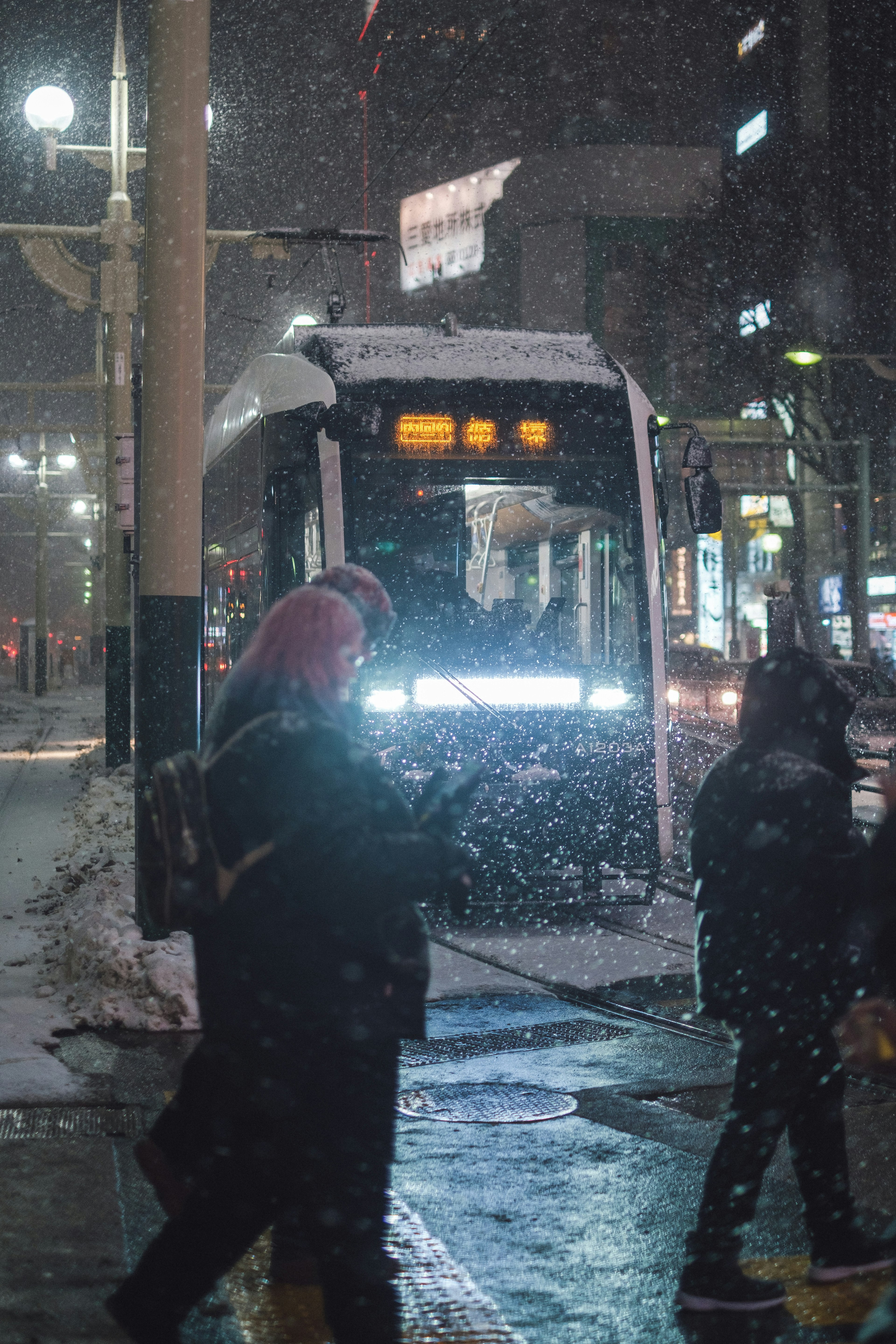 雪の降る夜の街でバスを待つ人々と雪に覆われたバス