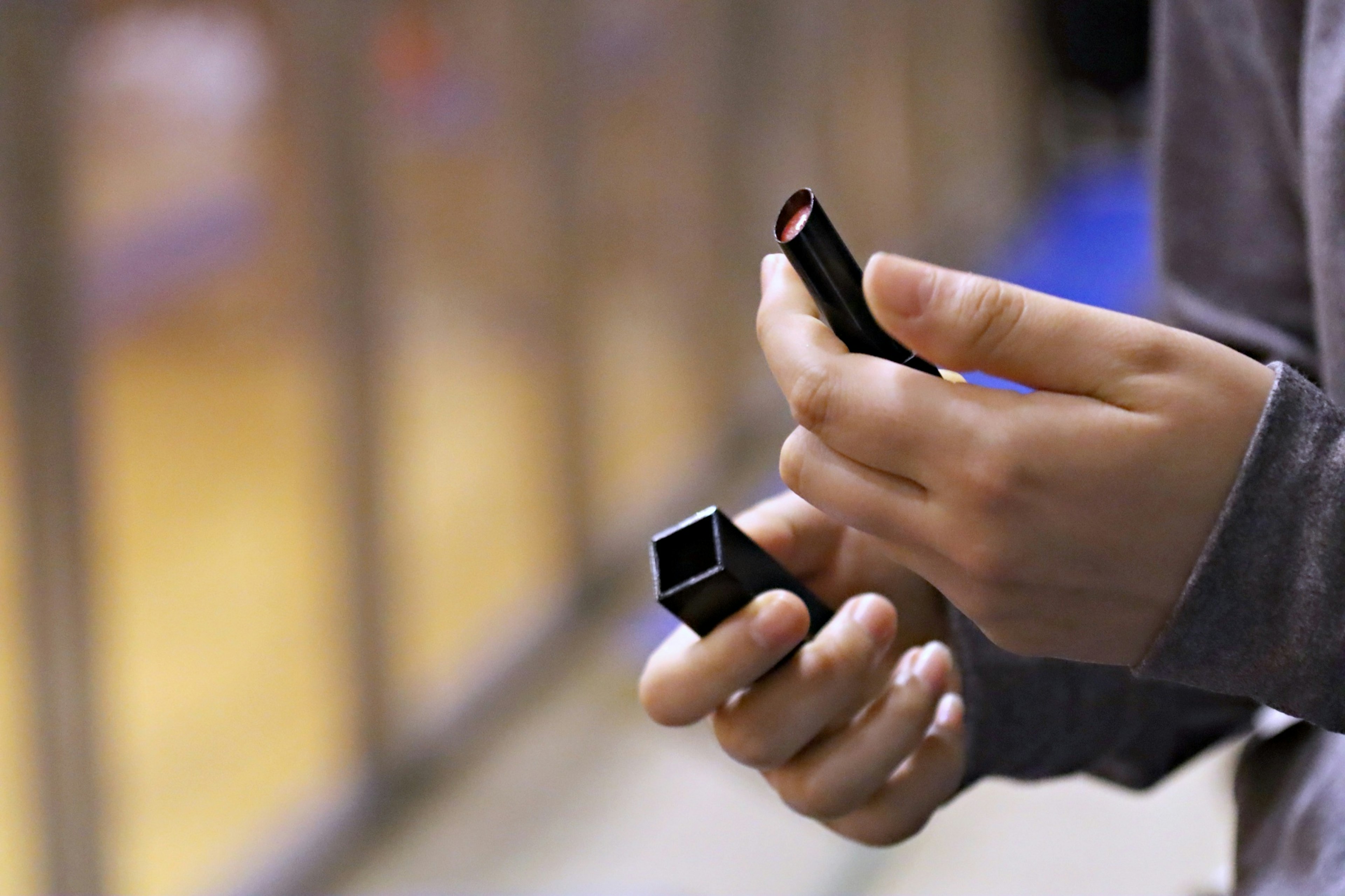 Primer plano de una mano sosteniendo un lápiz labial con un gimnasio borroso al fondo