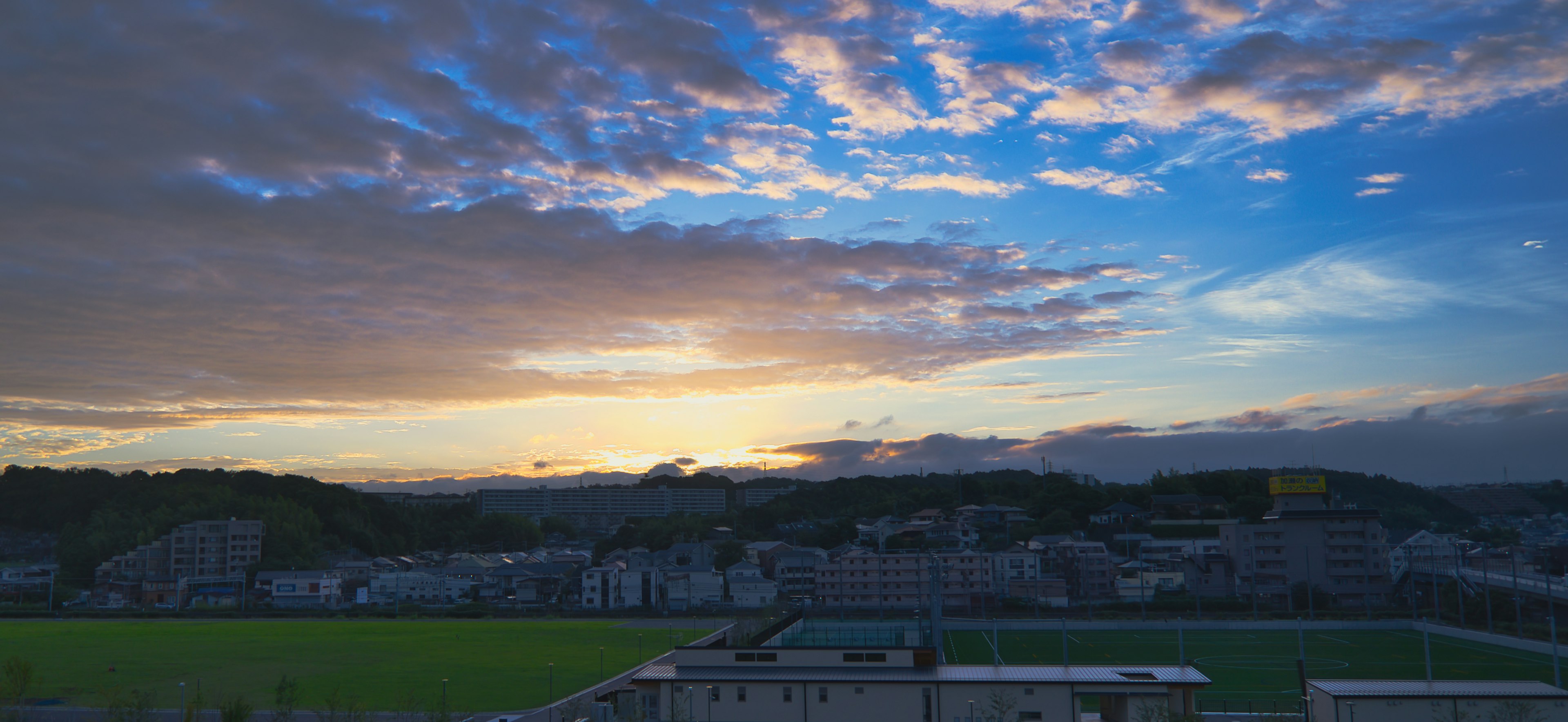 Paysage de coucher de soleil avec ciel bleu et nuages champ de gazon vert et bâtiments en vue