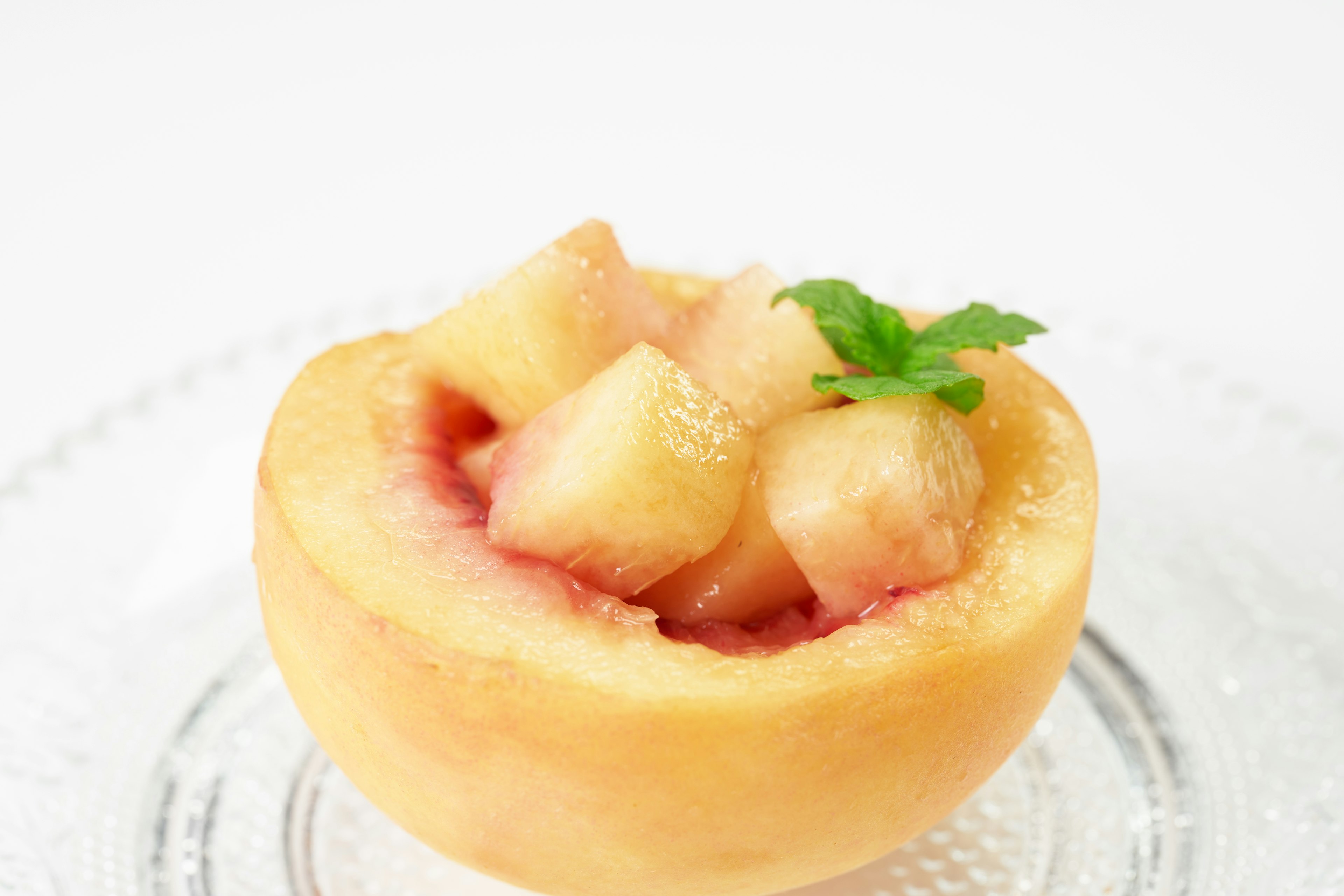 Half peach filled with diced peach and mint leaf on glass plate