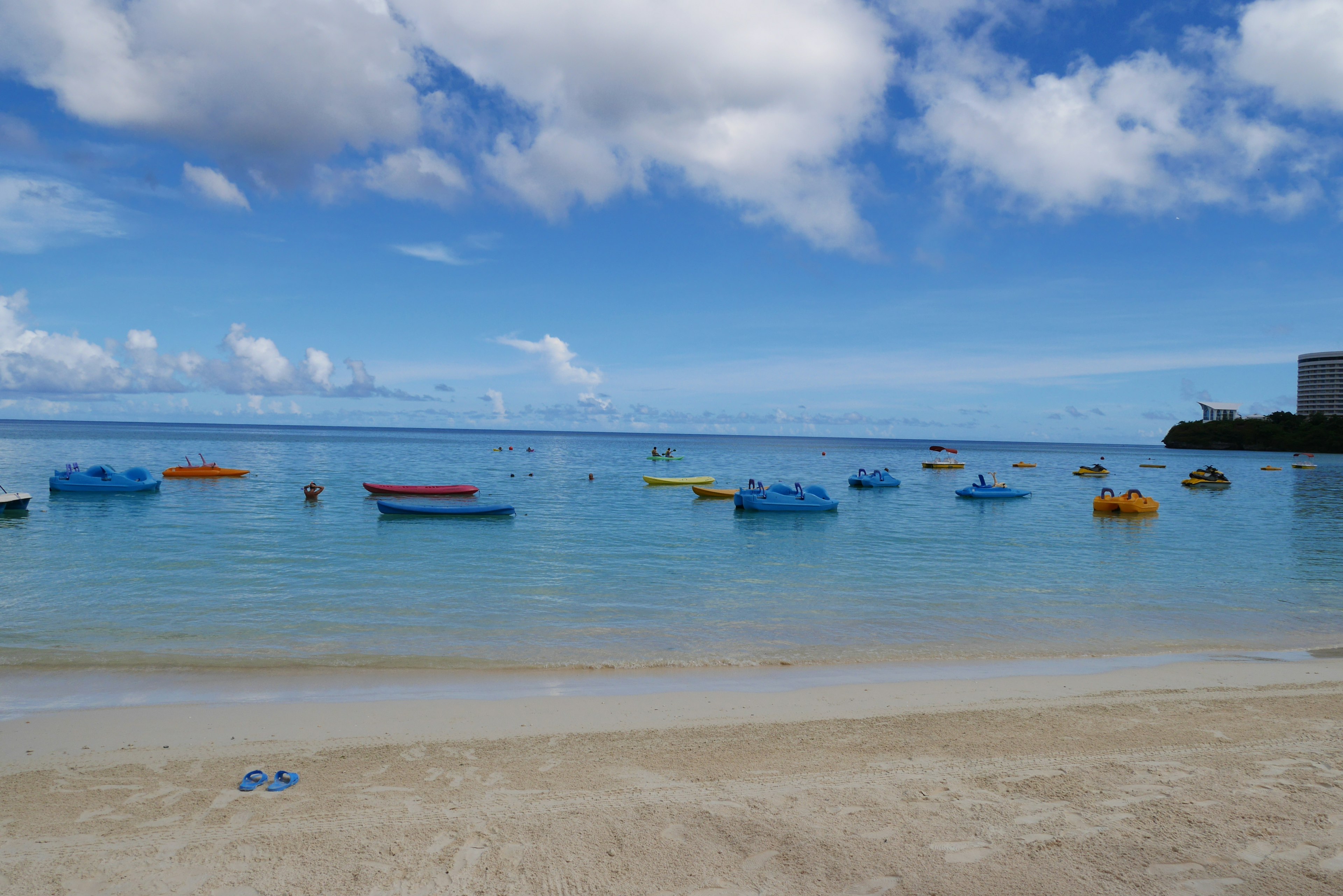 Colorful boats floating on calm water under a blue sky with clouds