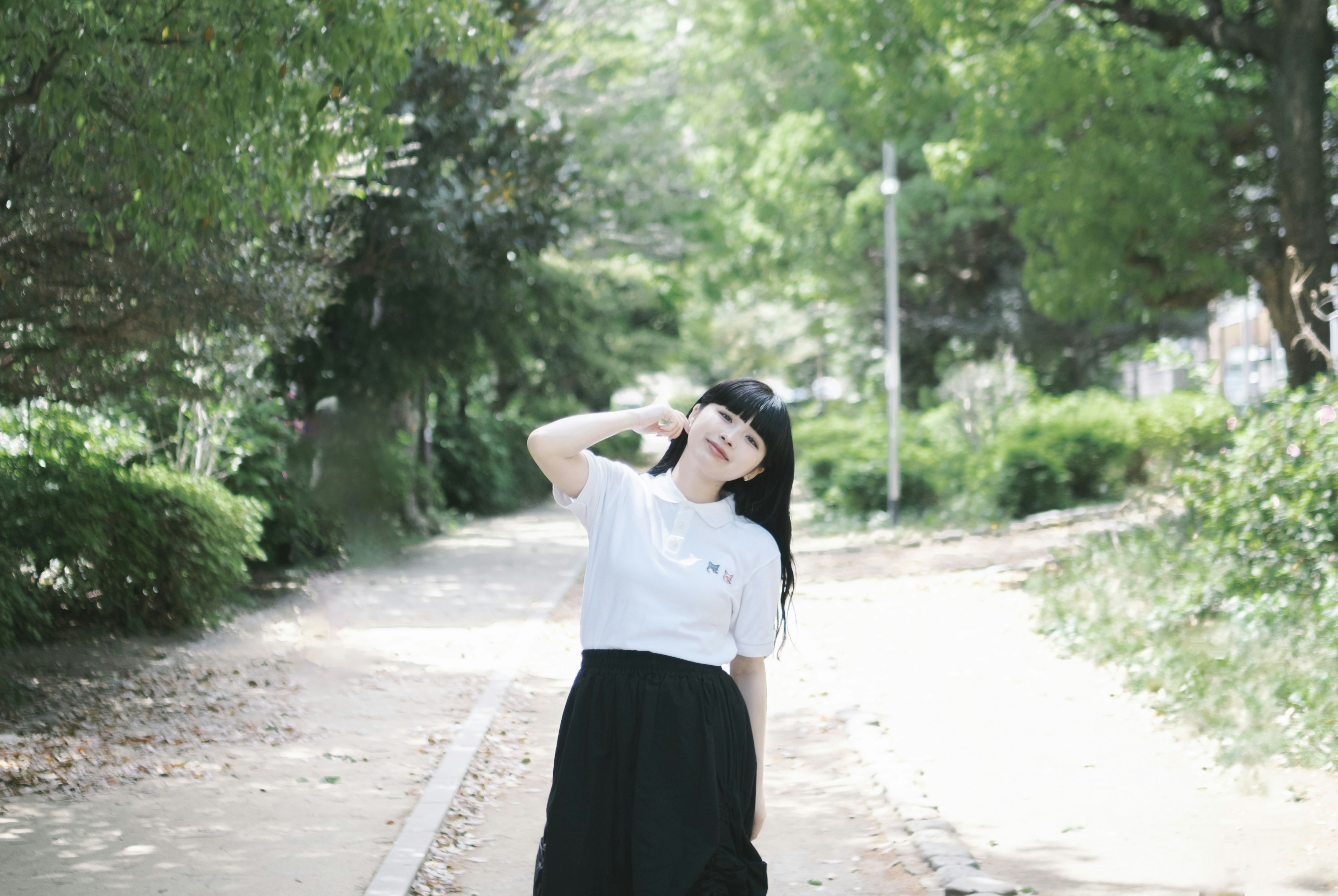 Woman posing on a park path surrounded by green trees