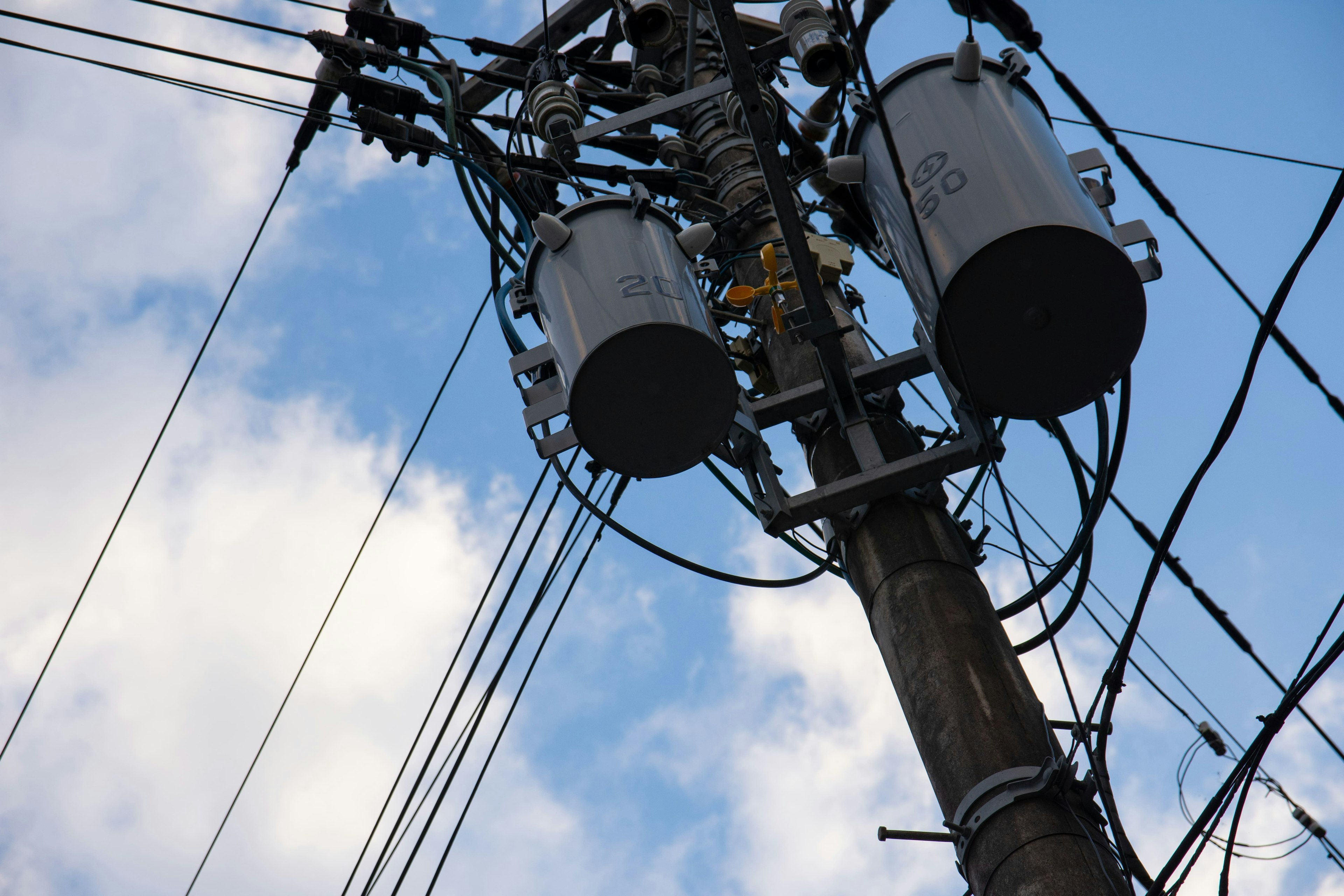 Close-up image of a utility pole with power lines against a blue sky and white clouds