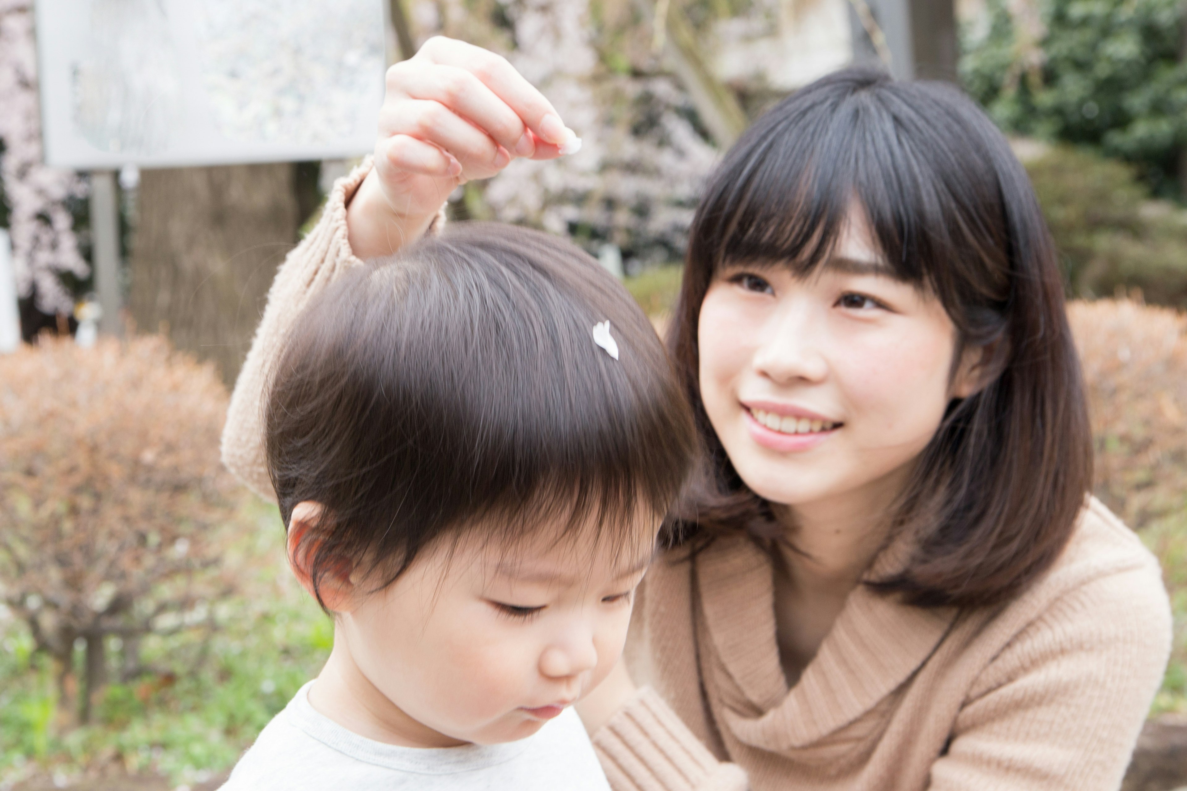 A mother placing a flower petal on her child's hair in a park