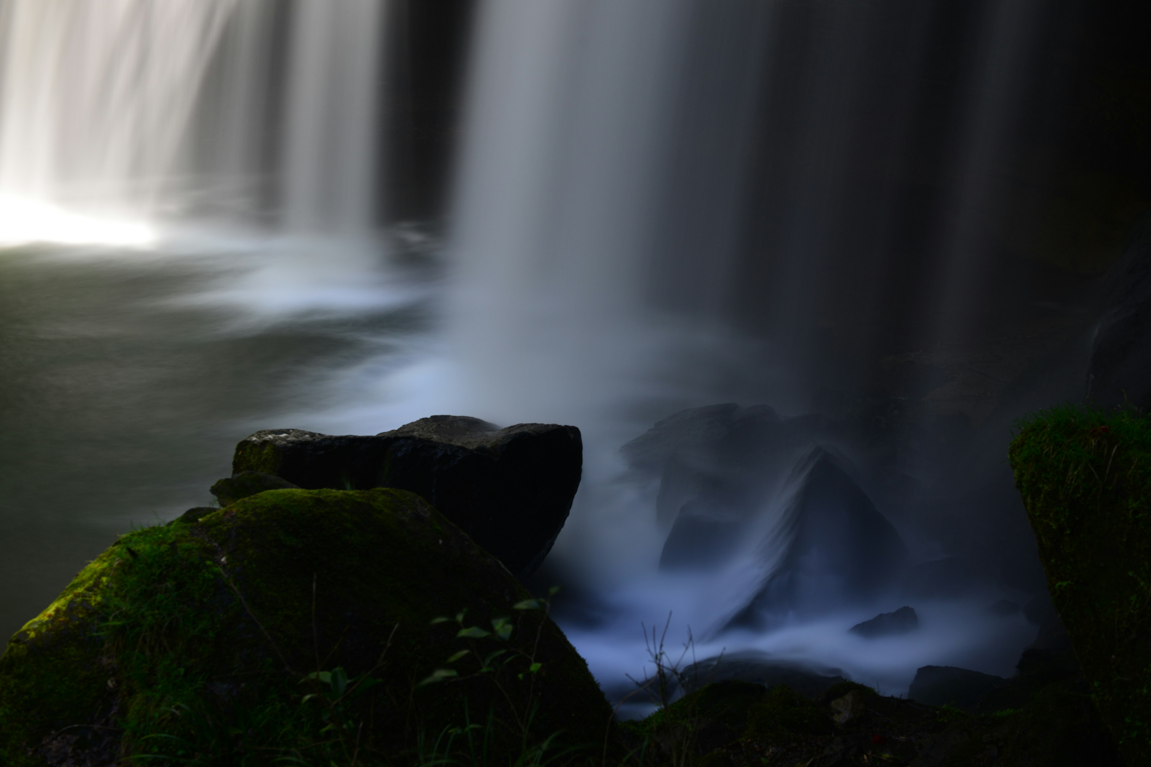 Nahaufnahme eines Steins neben einem Wasserfall mit fließendem Wasser