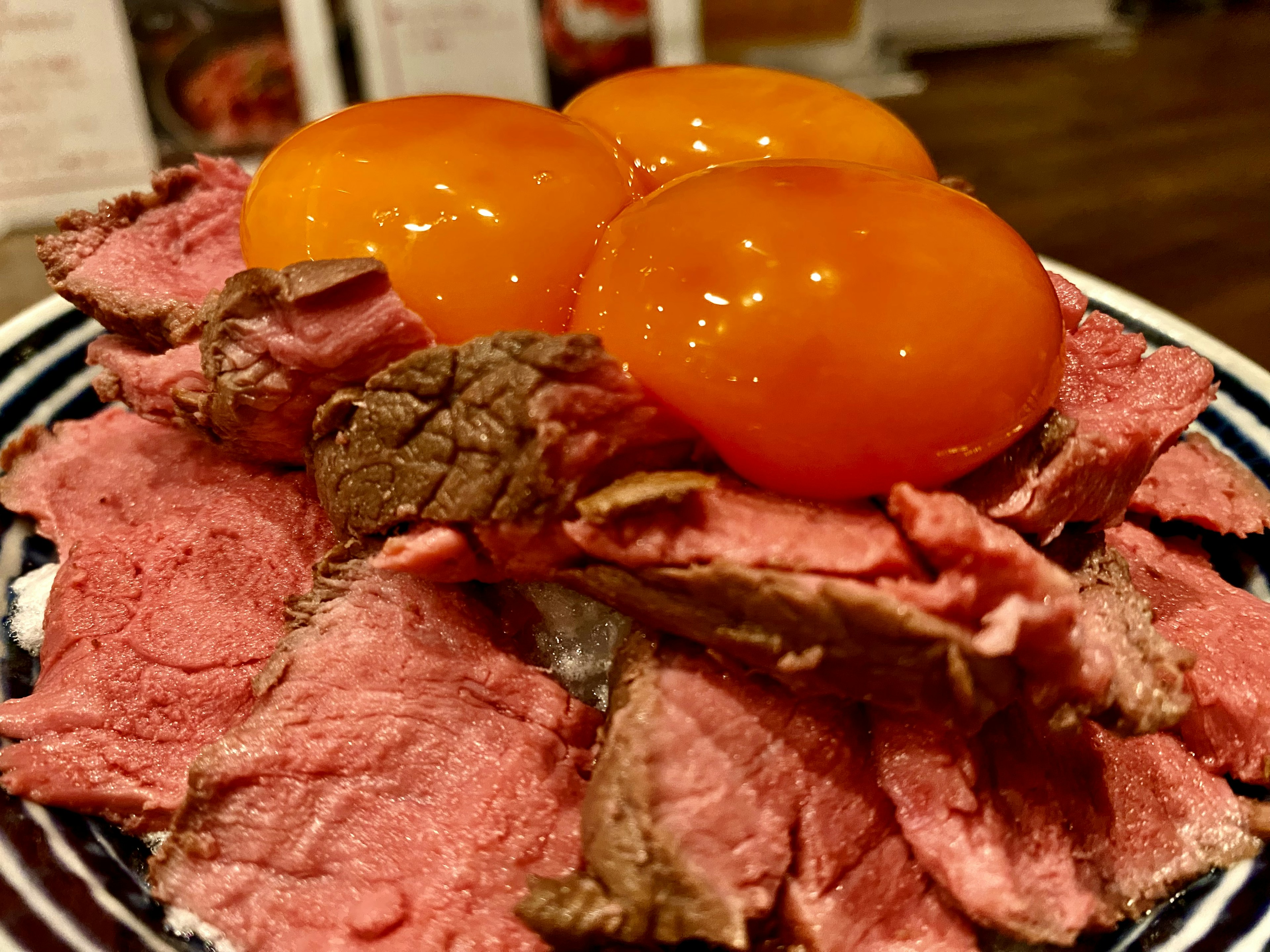 Un plato de carne asada en rodajas cubierto con tres yemas de huevo