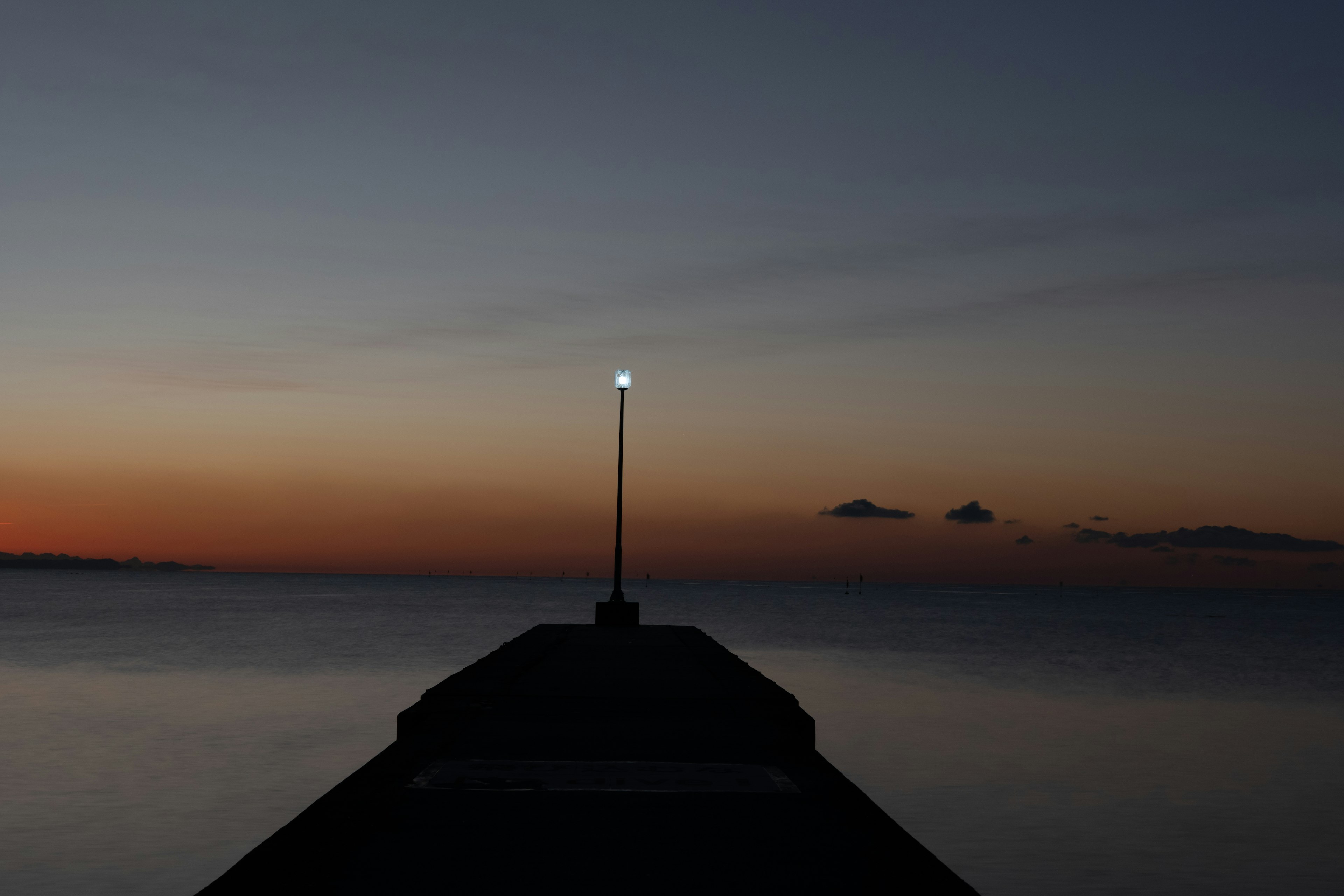 Bright lighthouse at the end of a pier during twilight