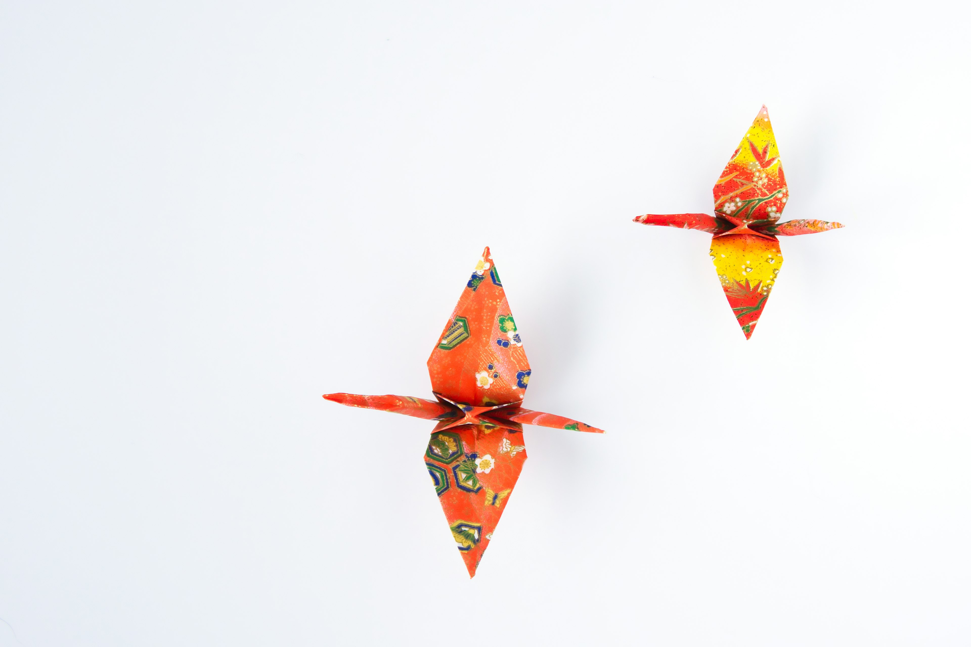 Two vibrant orange origami cranes displayed against a white background