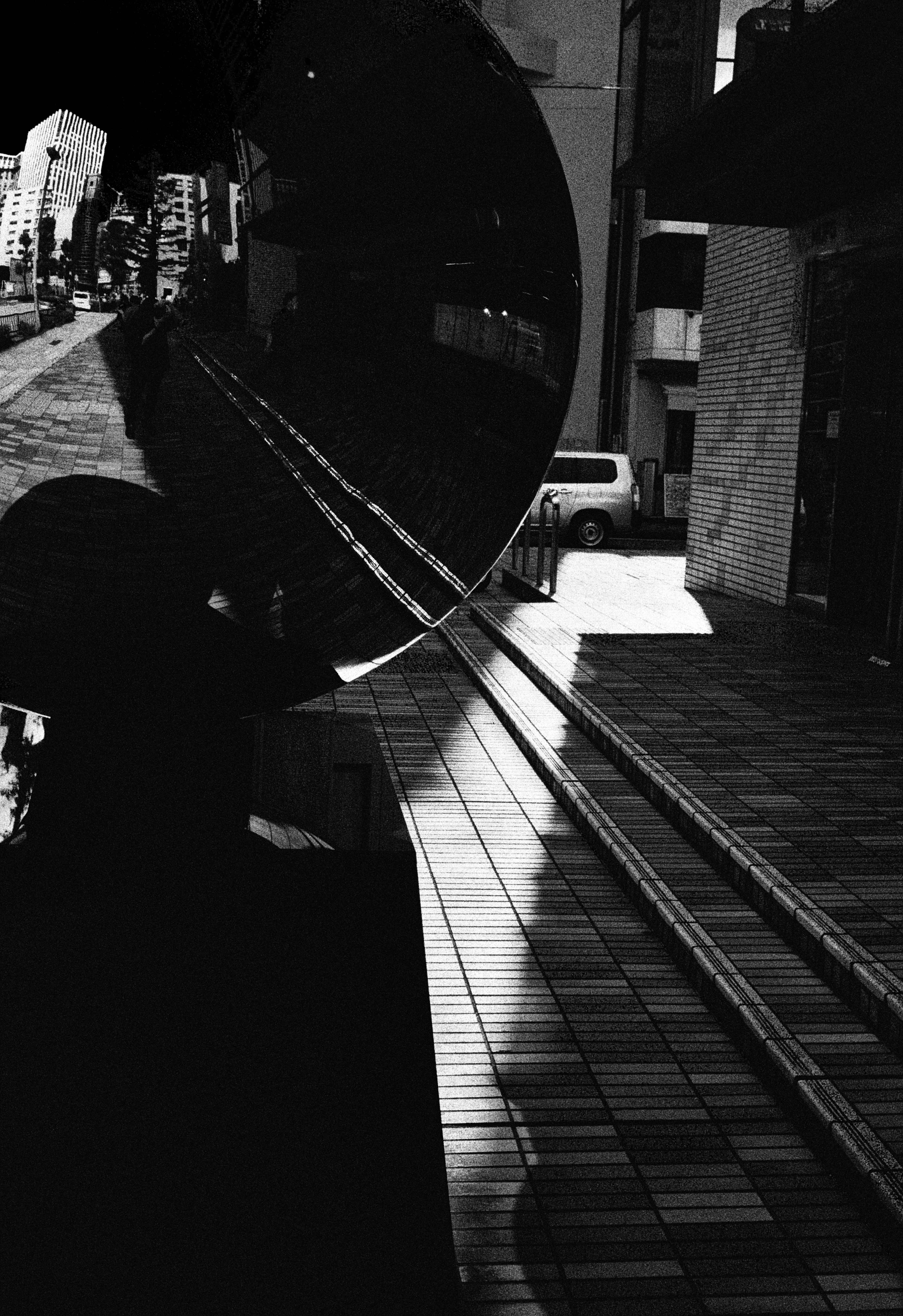 A person stands in front of a mirror reflecting a cityscape and train tracks in black and white