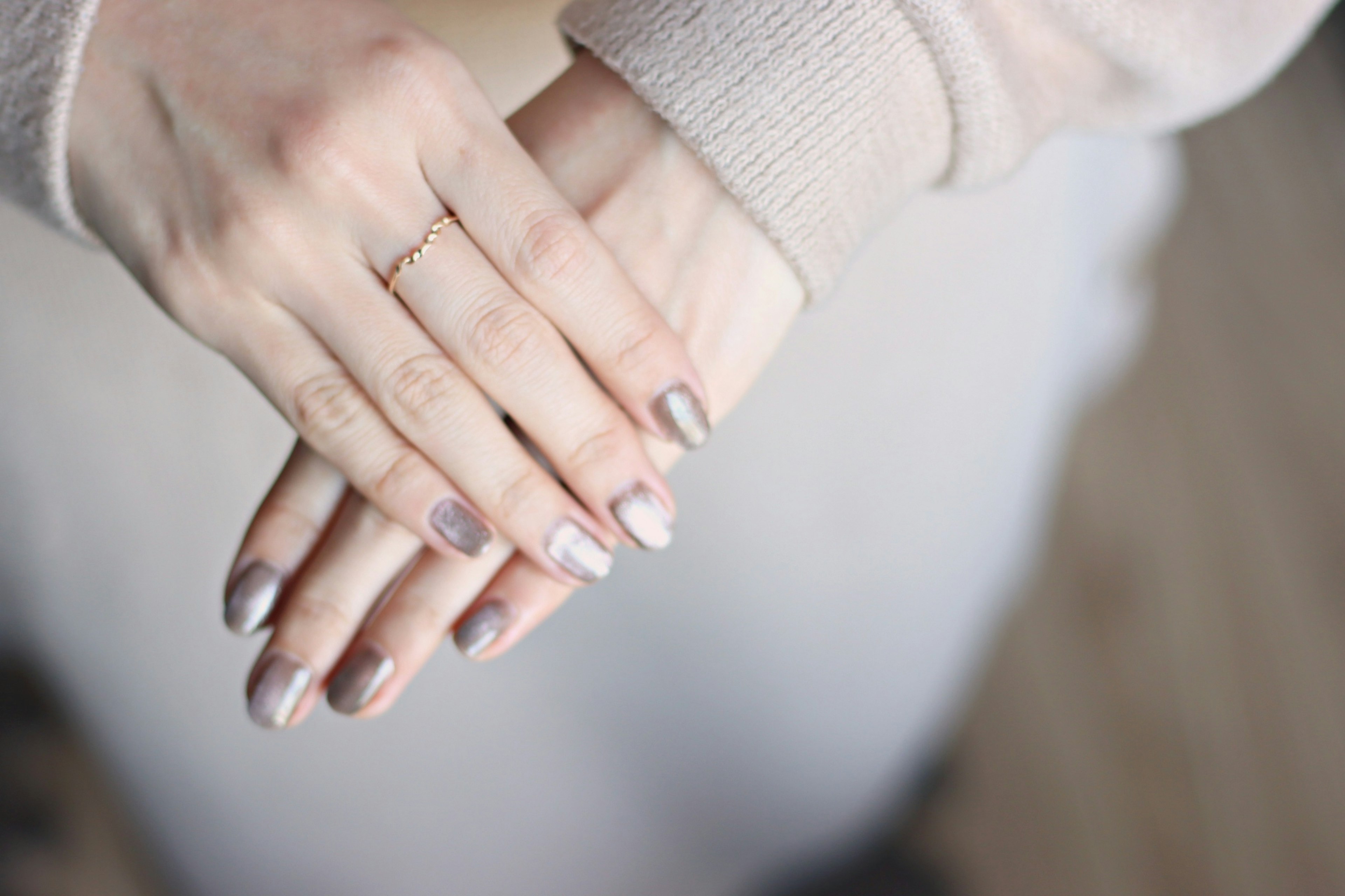 Close-up of elegantly manicured hands with neutral nail polish resting on a soft sweater