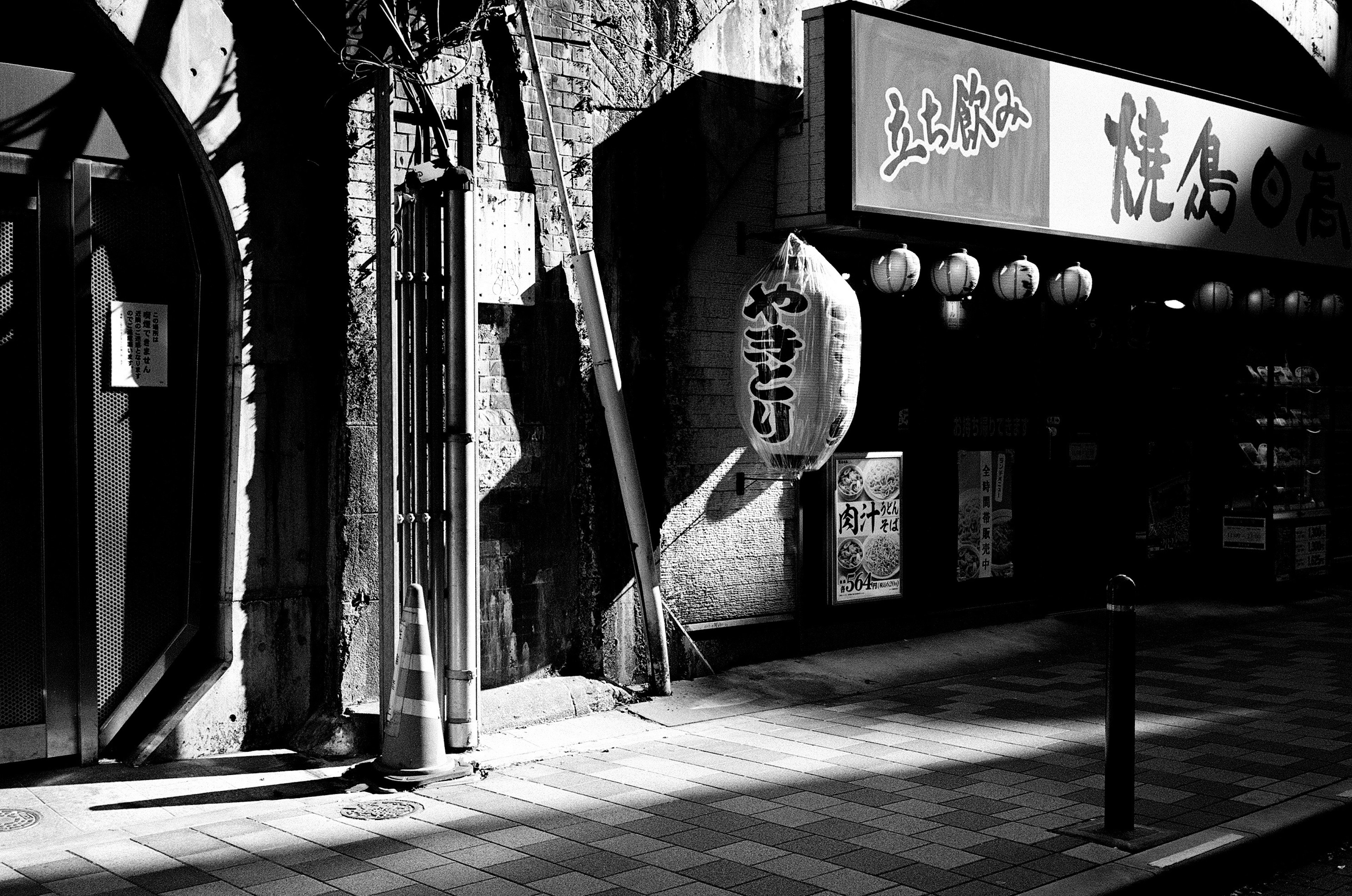 Coin de rue en noir et blanc avec un panneau d'izakaya japonais et des lanternes