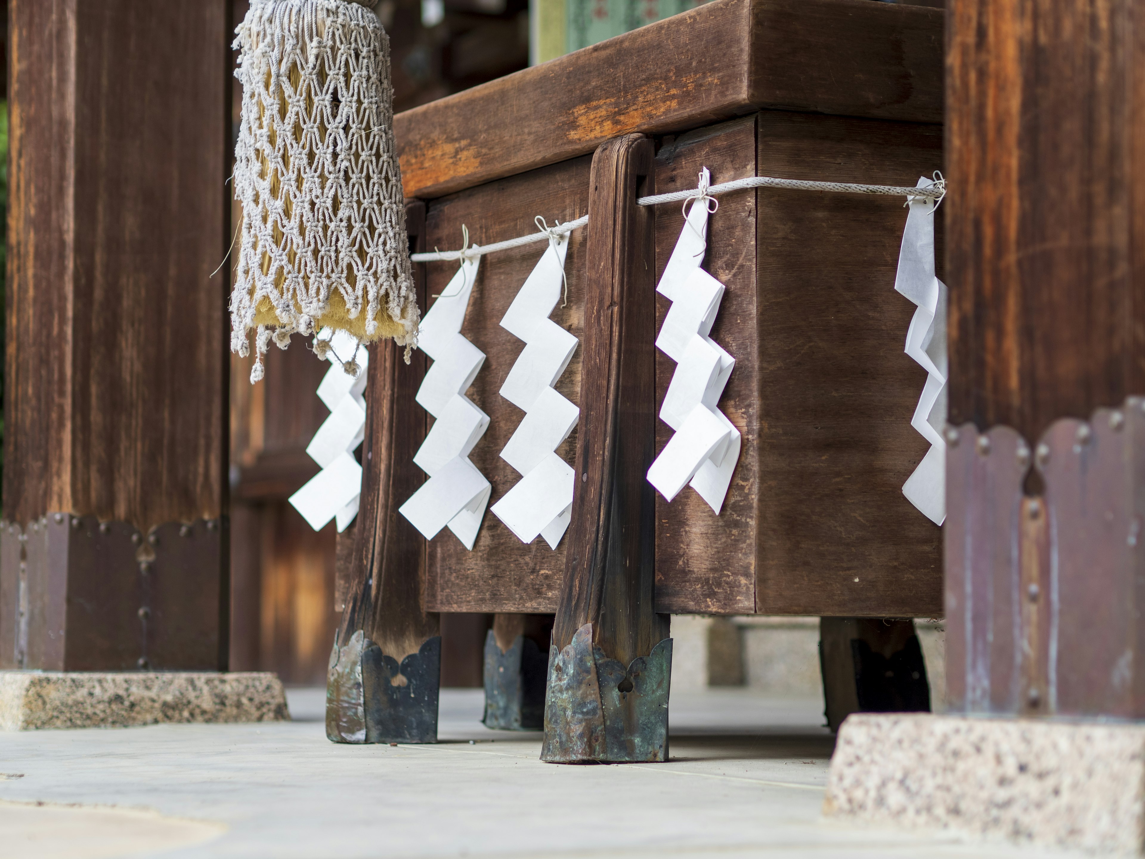 Details of white paper decorations and rope under a wooden shrine