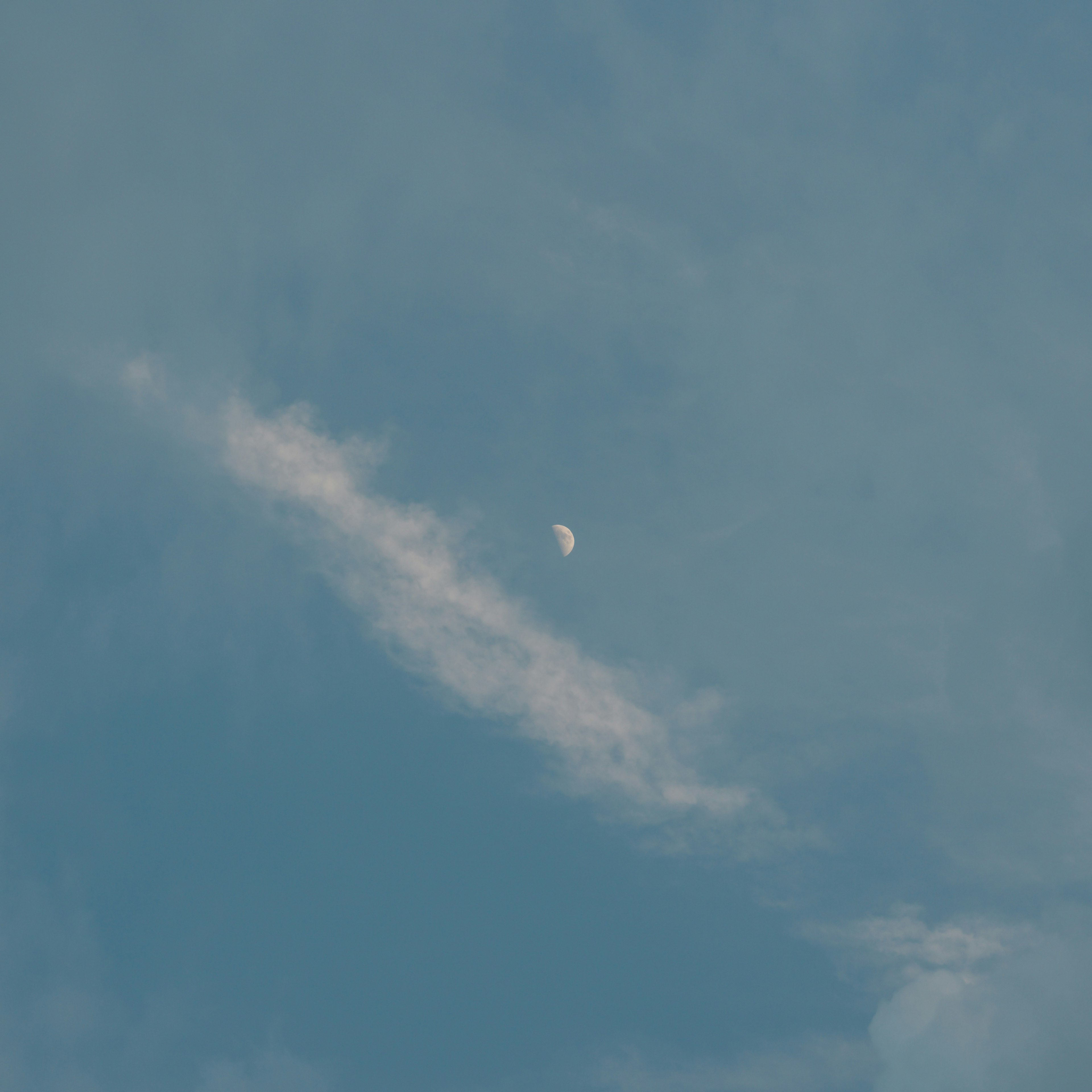 Luna parcial visible en un cielo azul con nubes delgadas