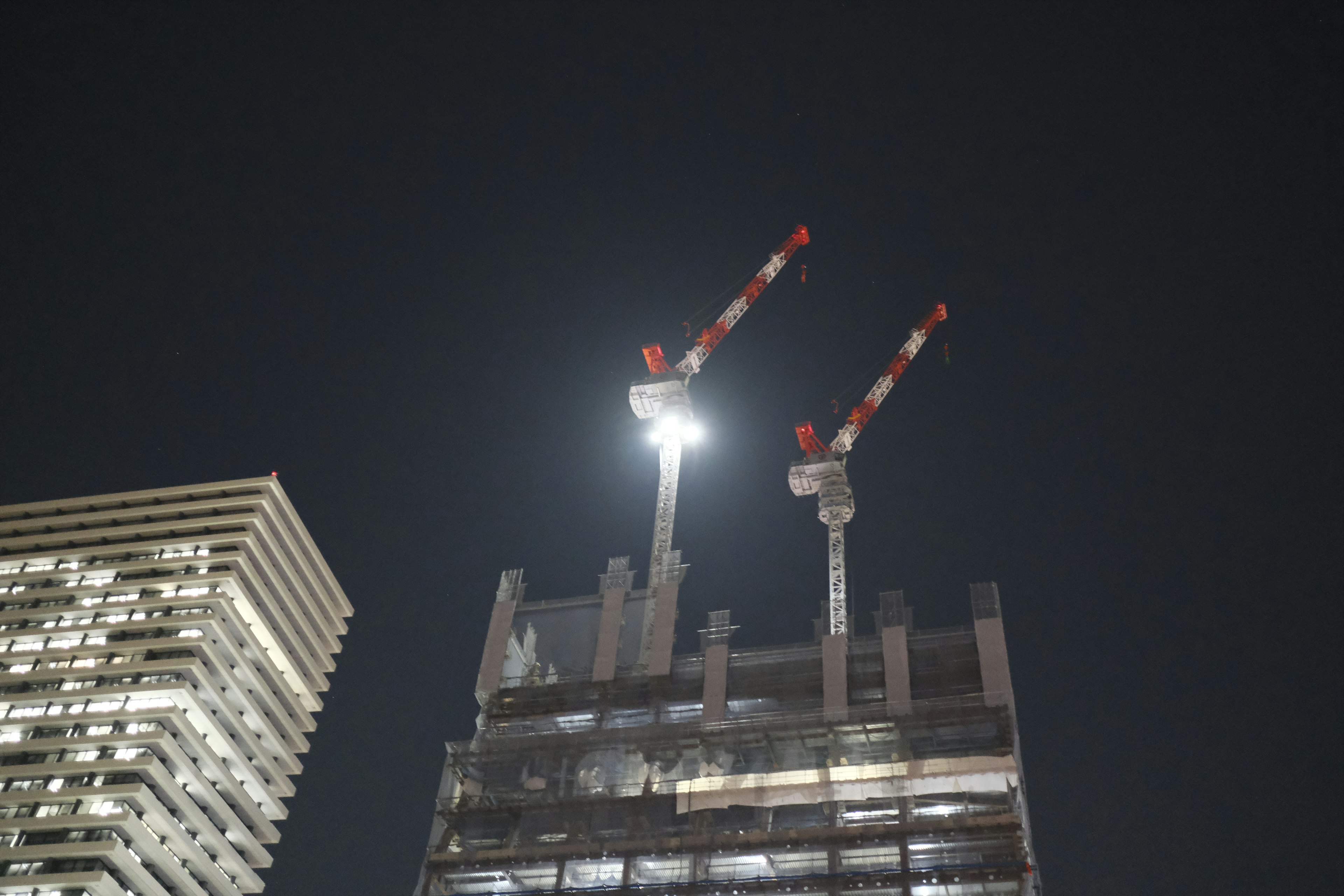 Cranes on a construction site at night with a building partially visible