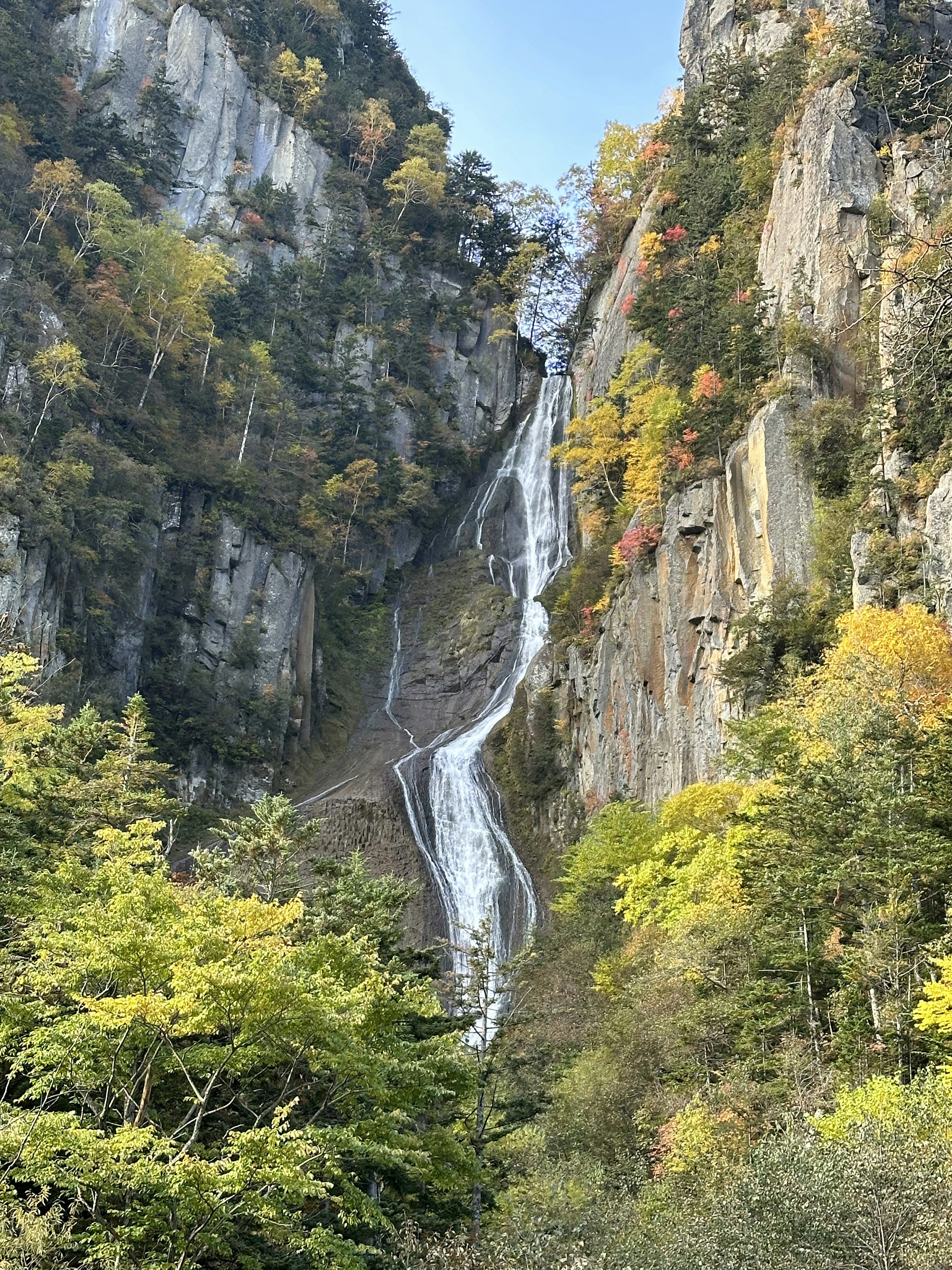 Paesaggio montano con una cascata circondata da fogliame autunnale