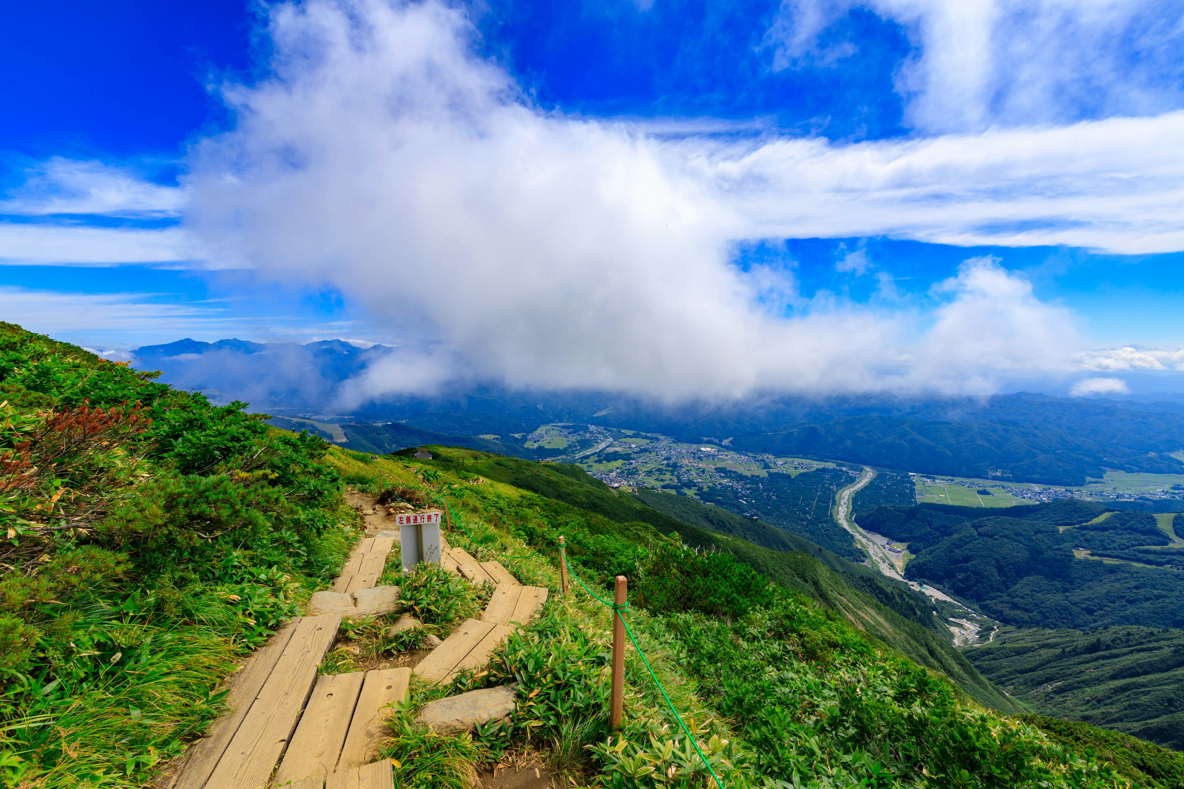 Paesaggio montano con cielo blu e nuvole prato verde e sentiero in legno