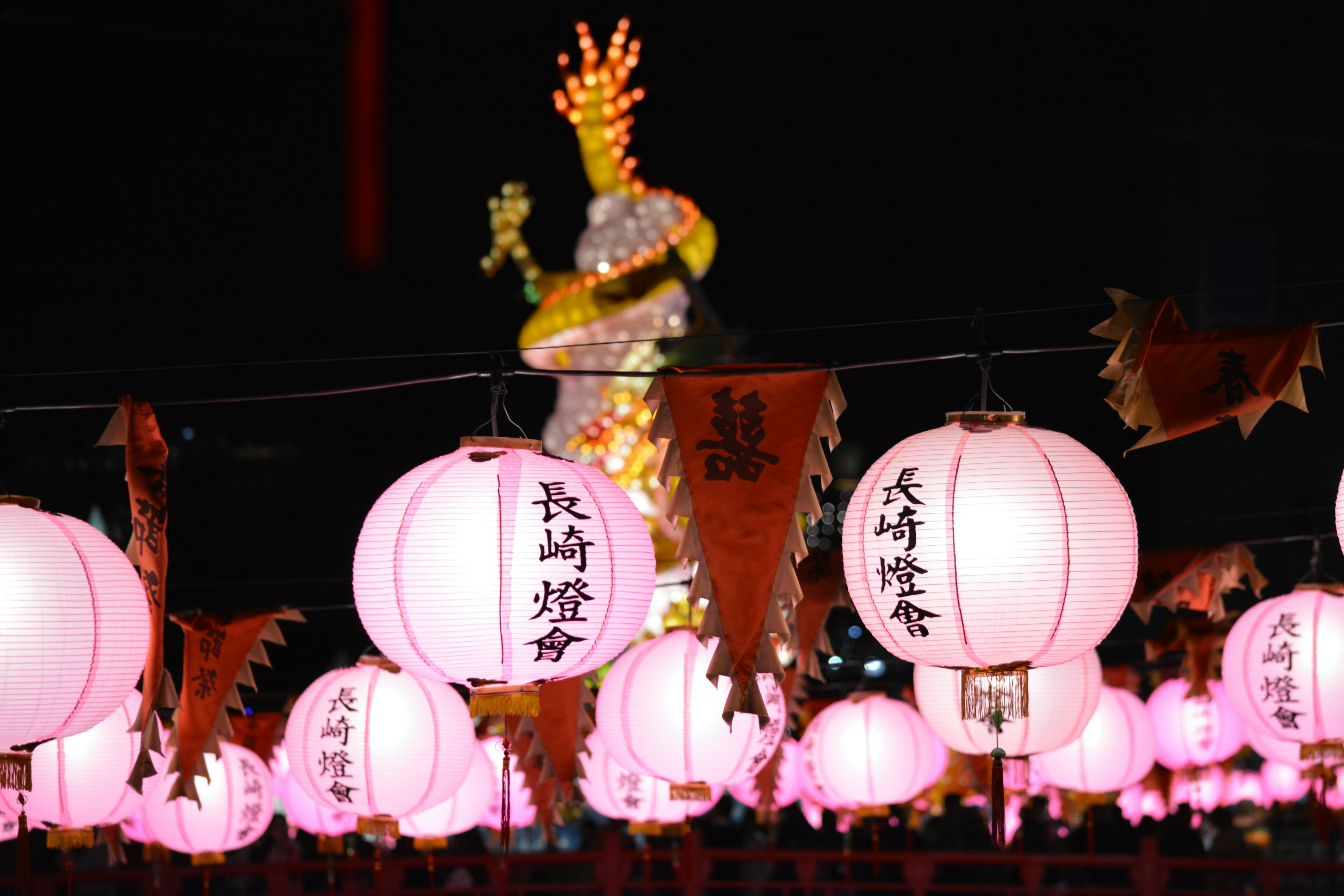 Pink lanterns illuminated at night with a colorful decoration in the background