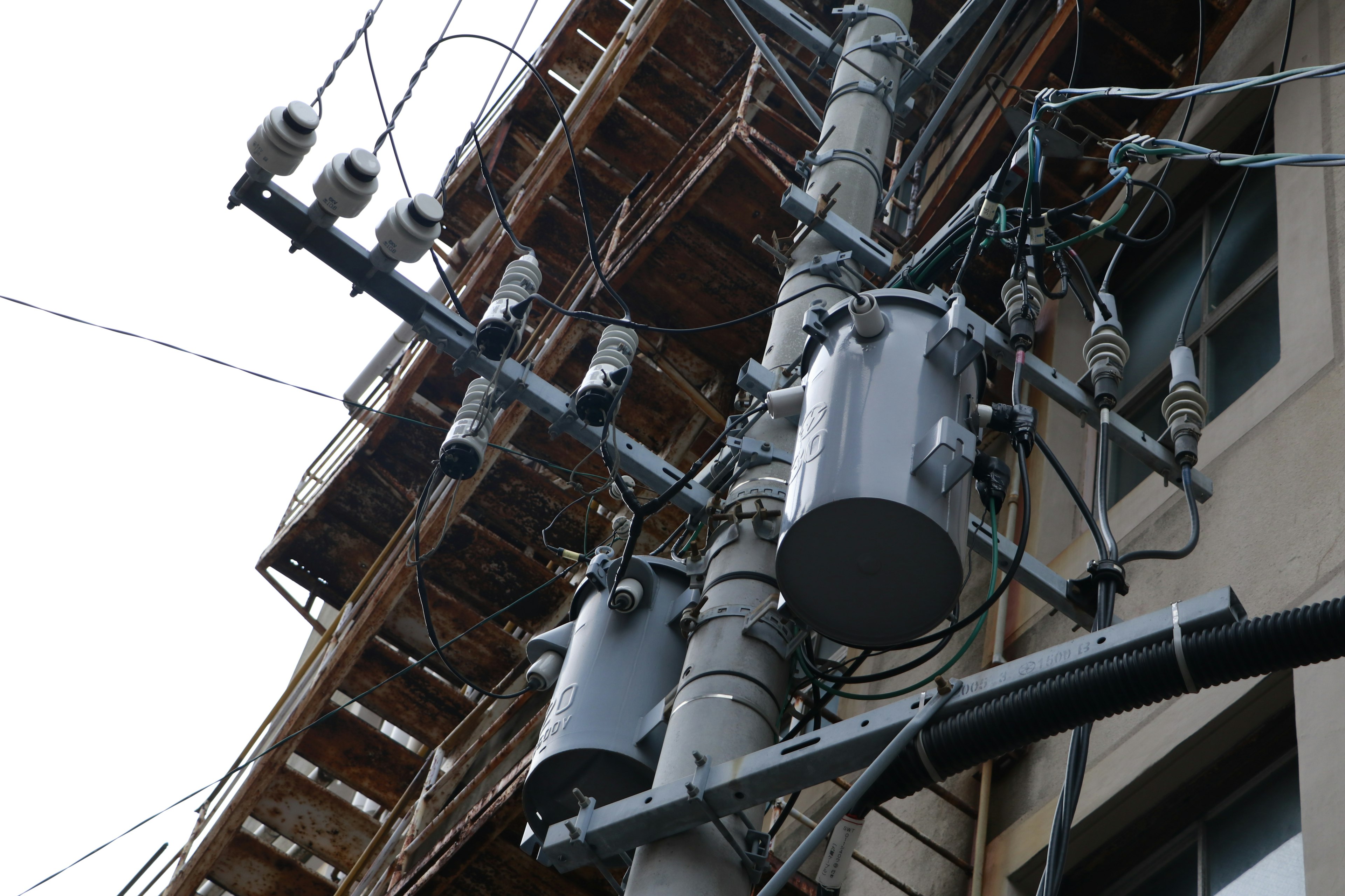 Close-up of utility poles and transformers next to a building