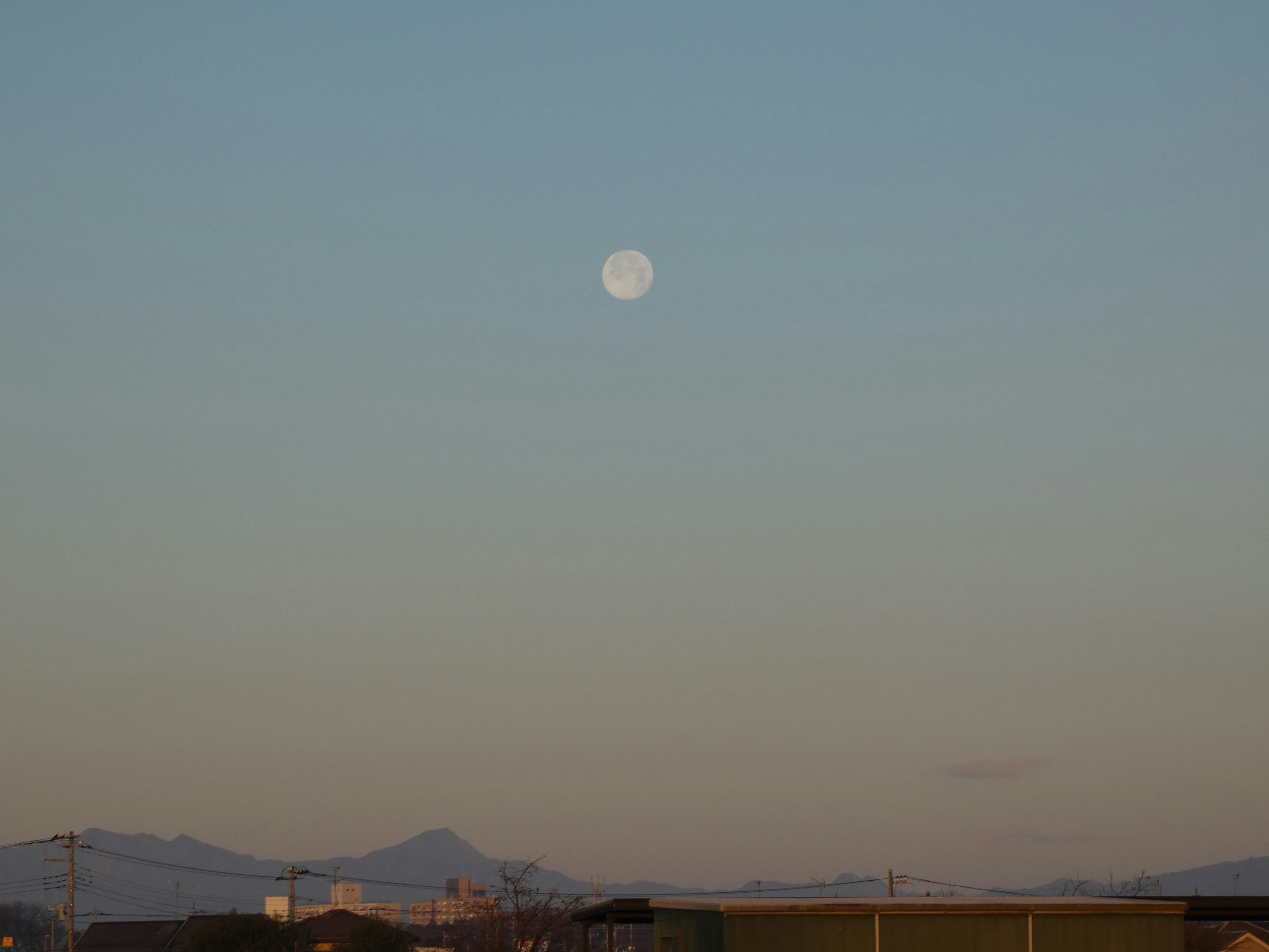 Full moon in a clear blue sky with distant mountains