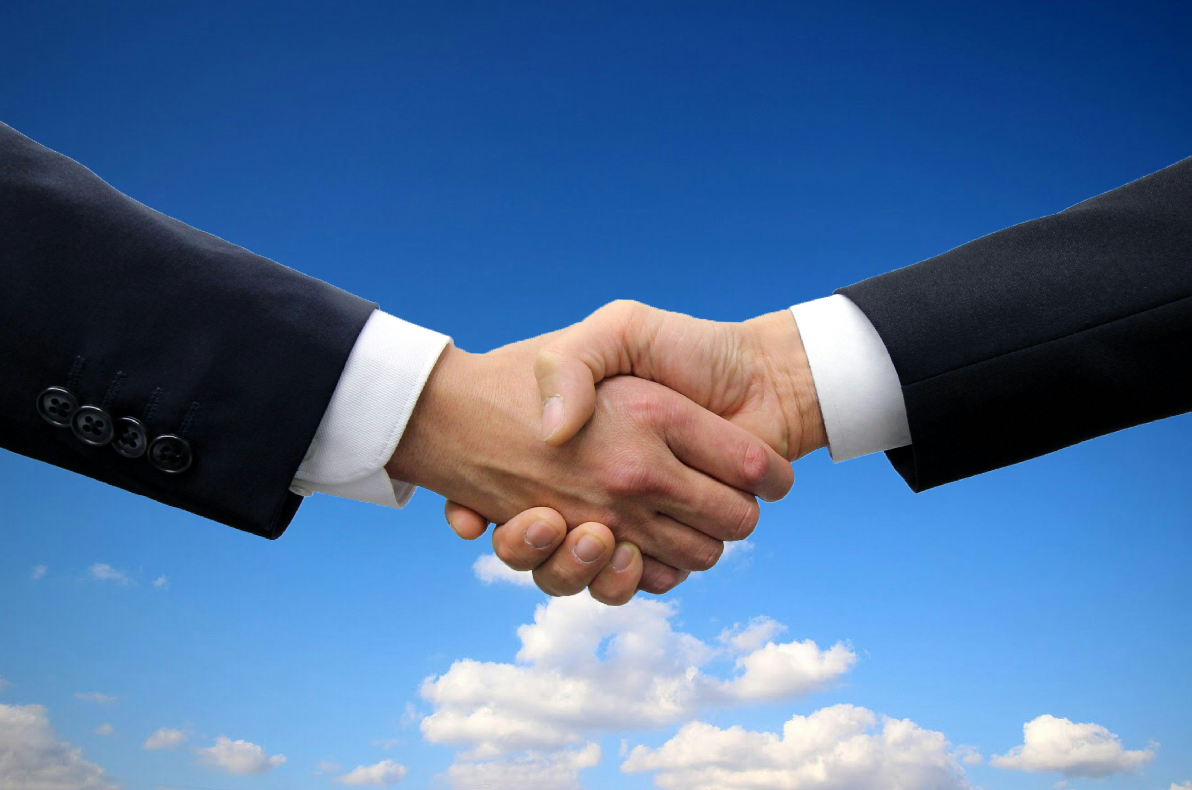 Two business hands shaking under a blue sky