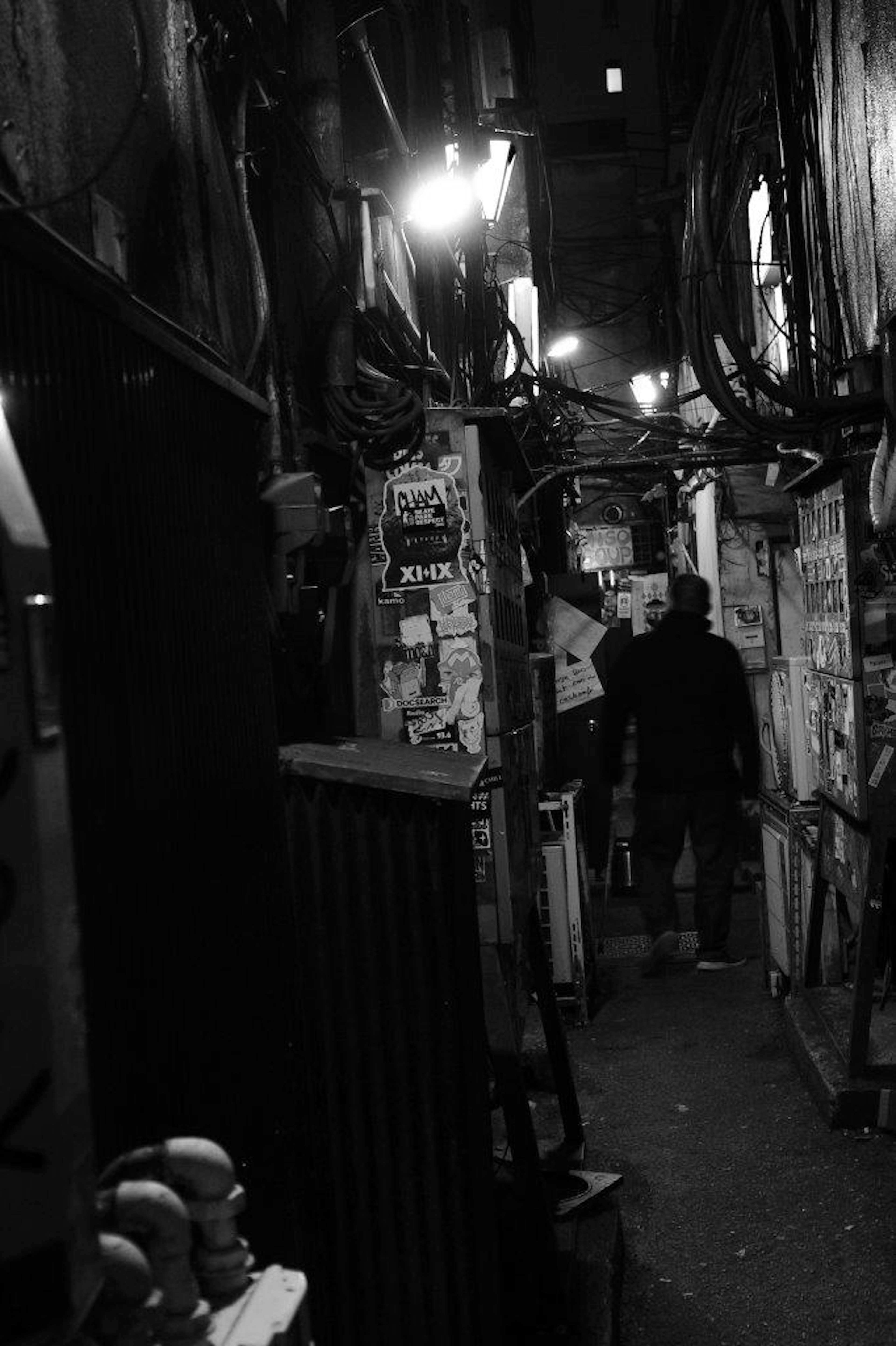 Black and white photo of a narrow alley with a silhouette of a person and old streetlights