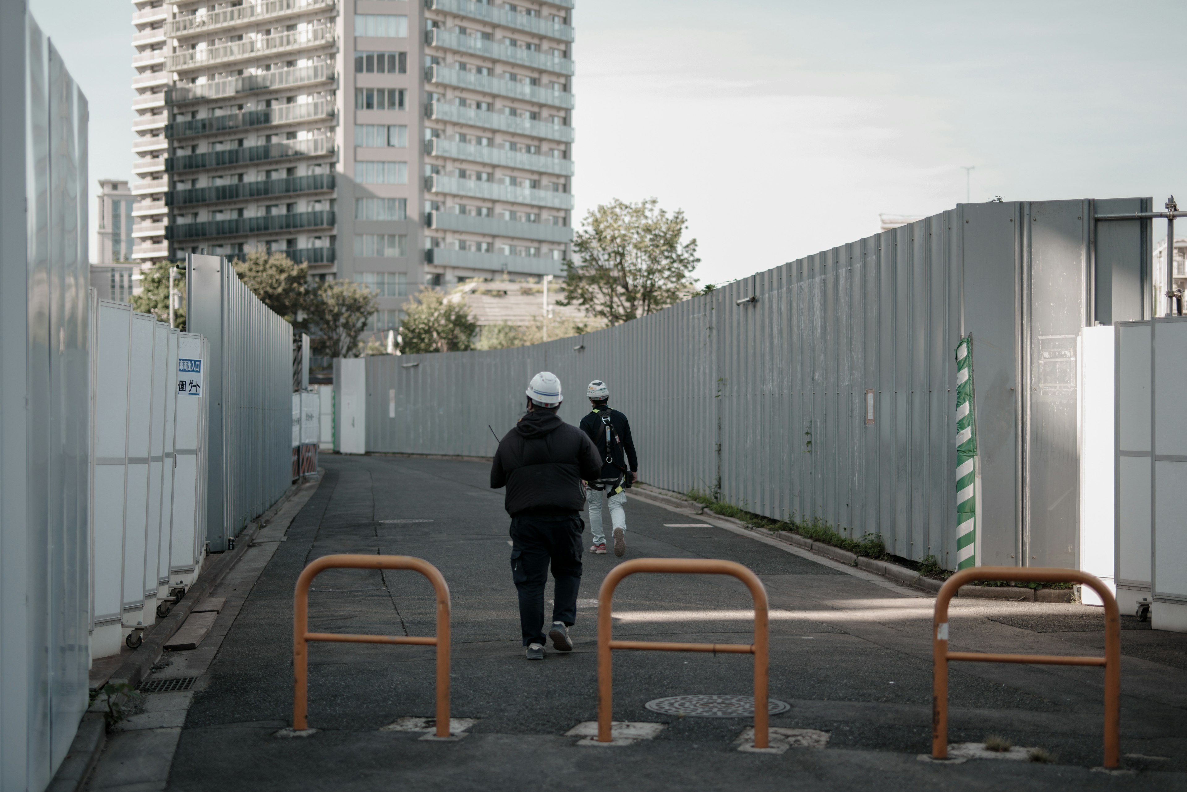 Deux ouvriers marchant sur un chemin de chantier avec un immeuble en arrière-plan