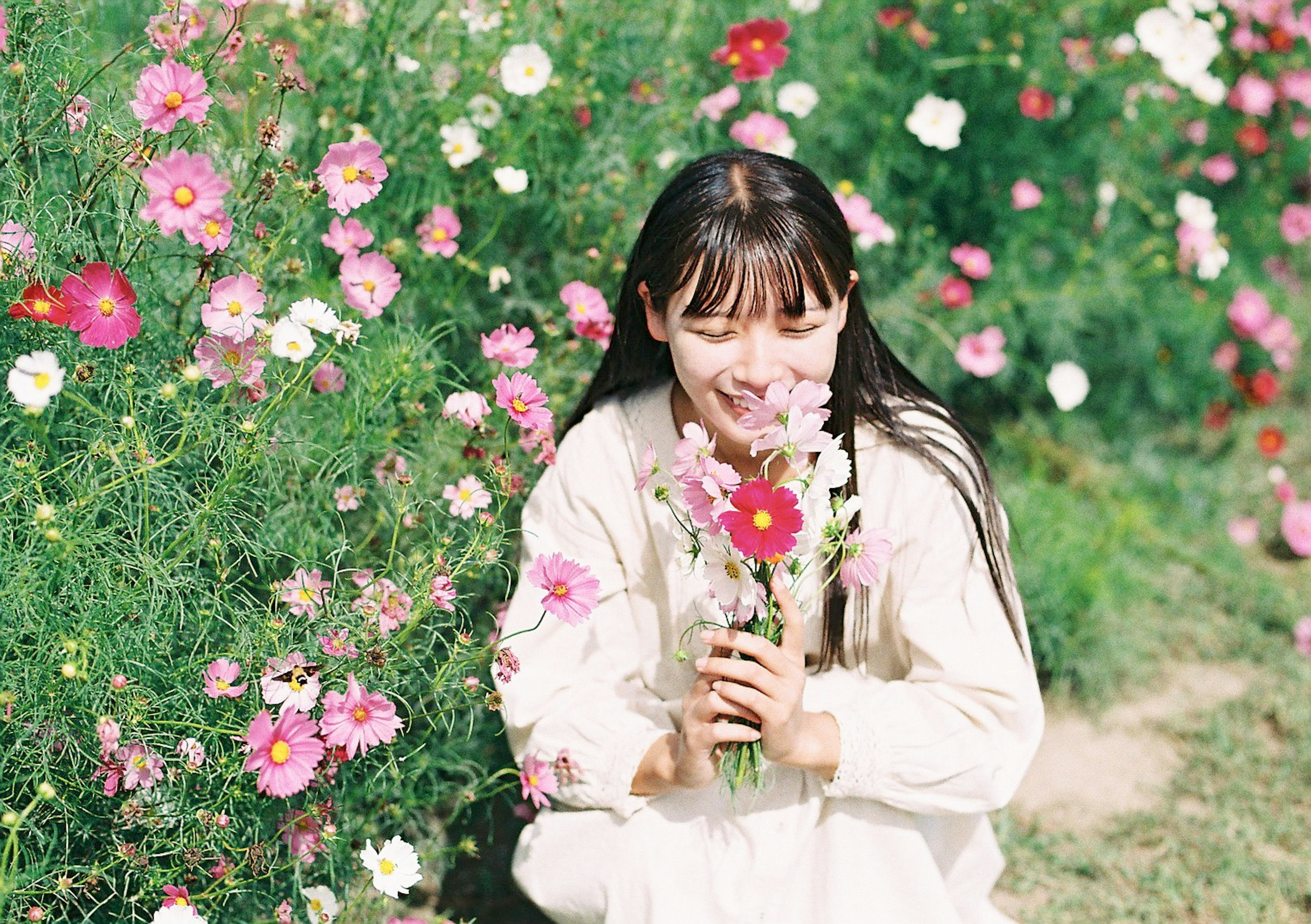 Una niña sonriendo mientras sostiene un ramo rodeada de flores coloridas