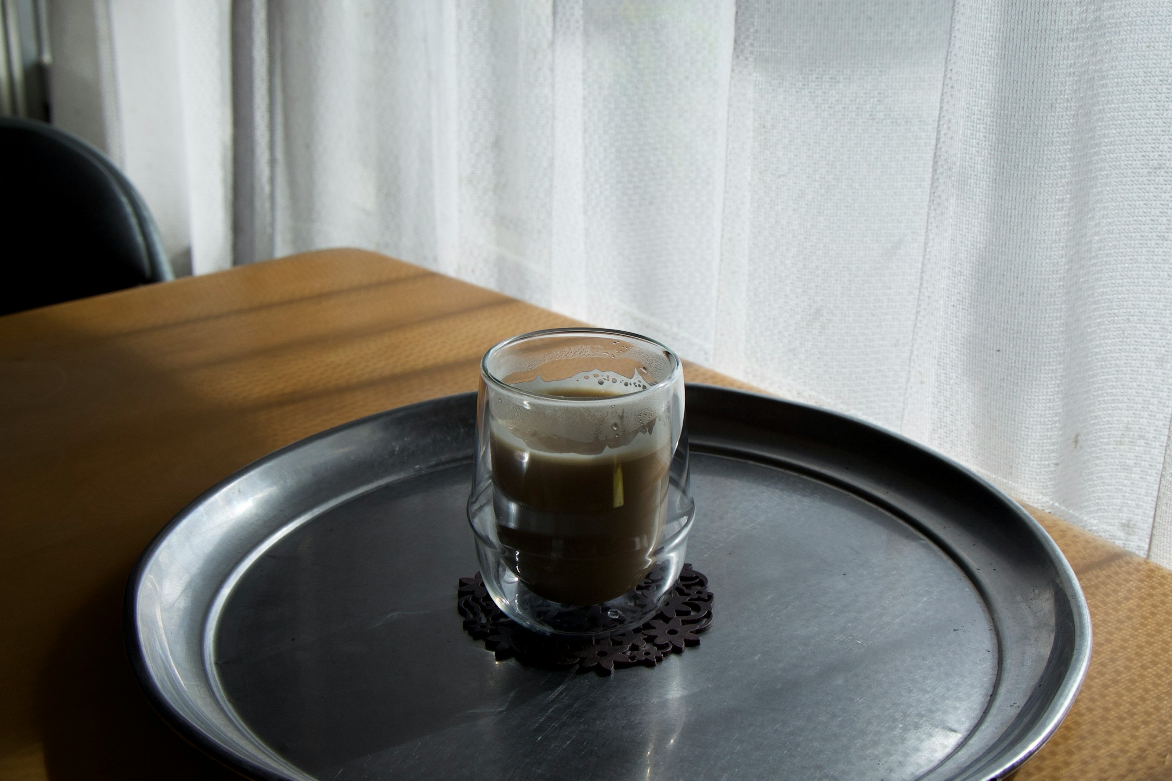 A transparent cup with a drink sits on a silver tray