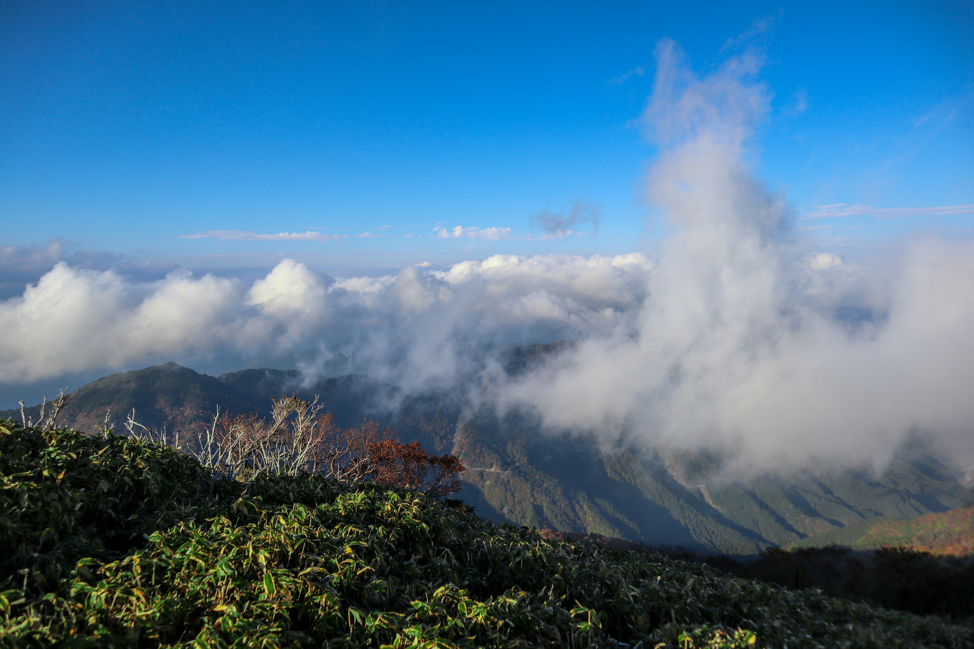 Stunning view from a mountain peak featuring a blue sky and cloud-covered landscape