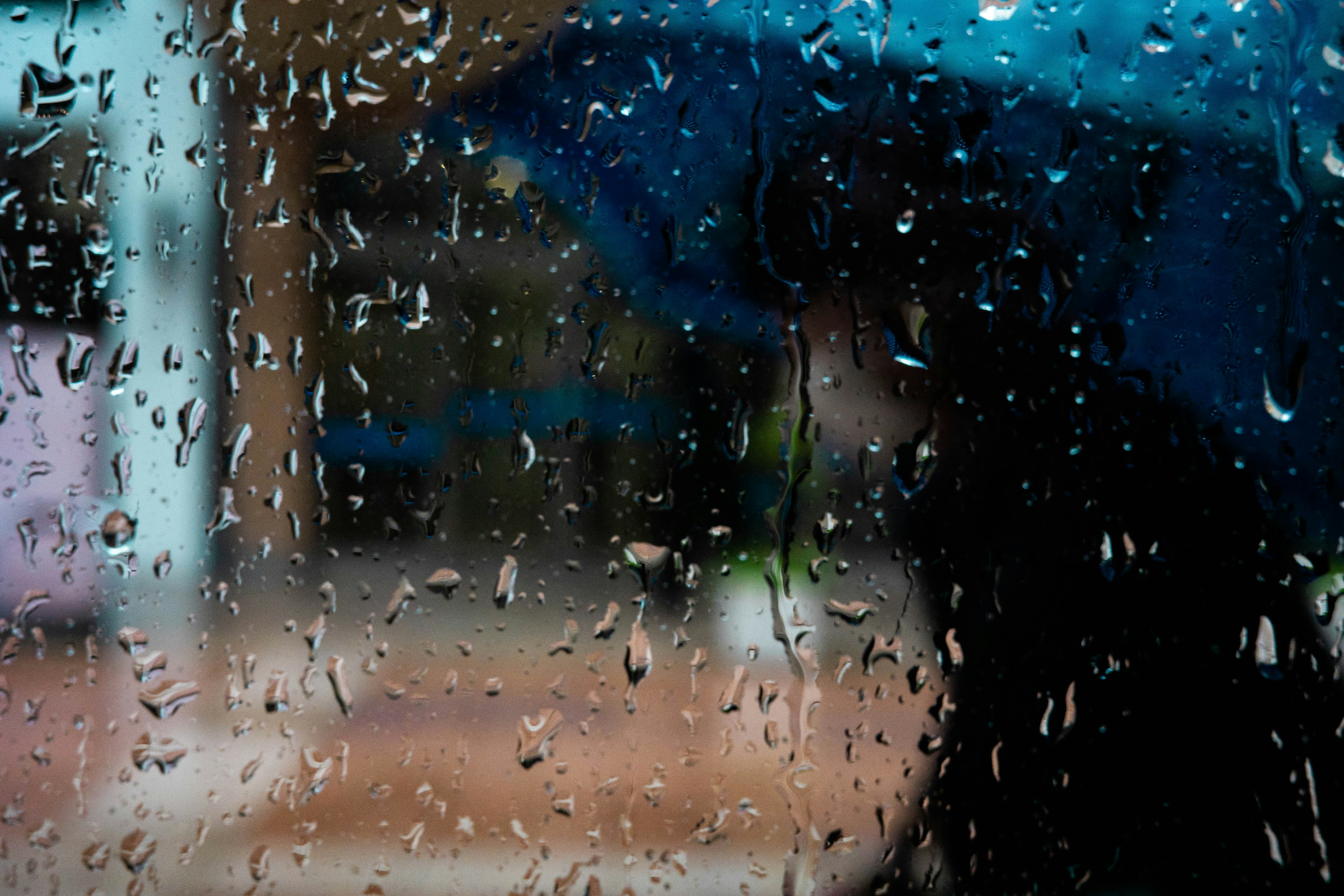 雨の中、青い傘を持った人影が窓越しに見える