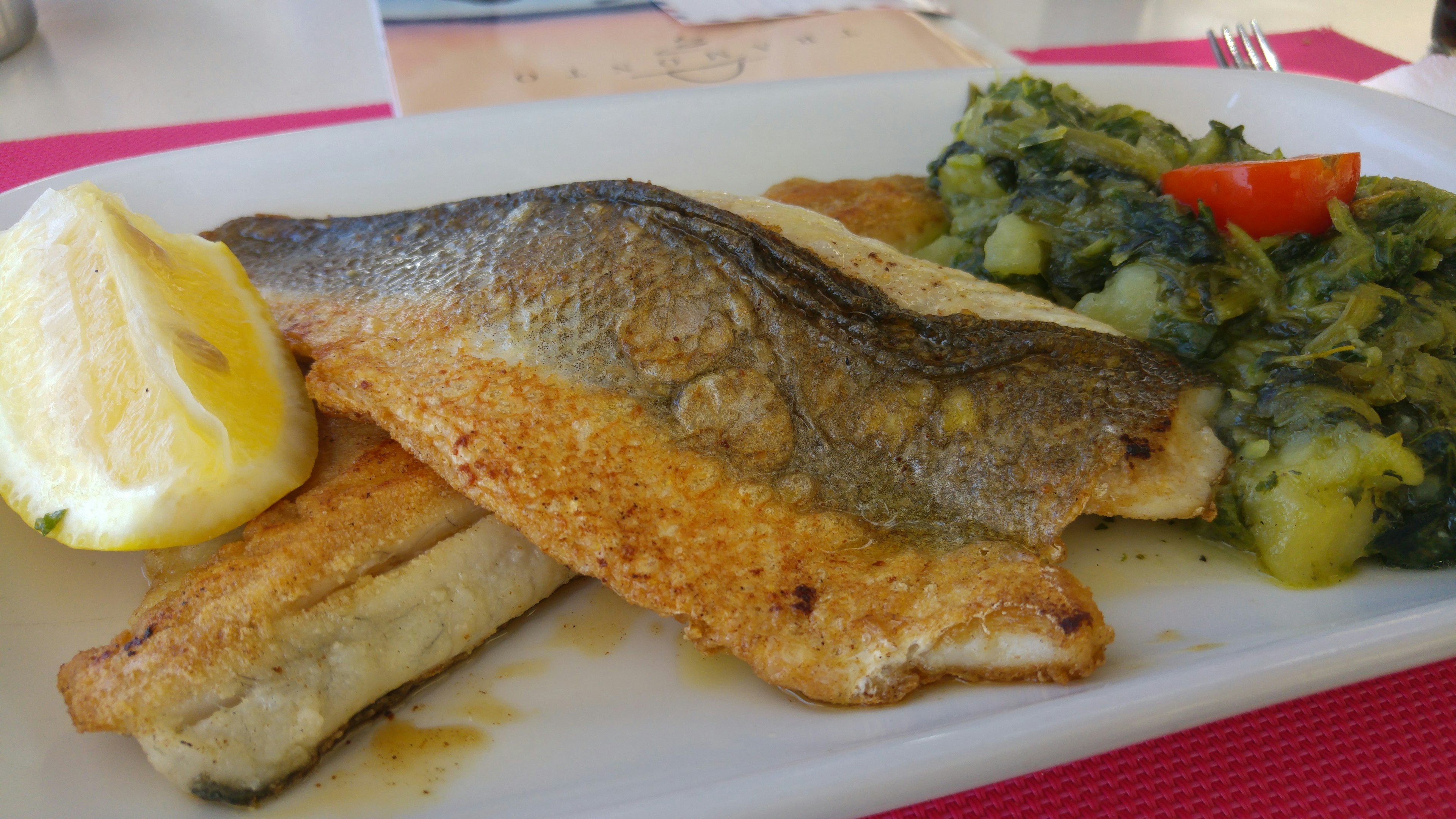 Pescado a la parrilla servido con rodajas de limón y verduras verdes con tomate rojo