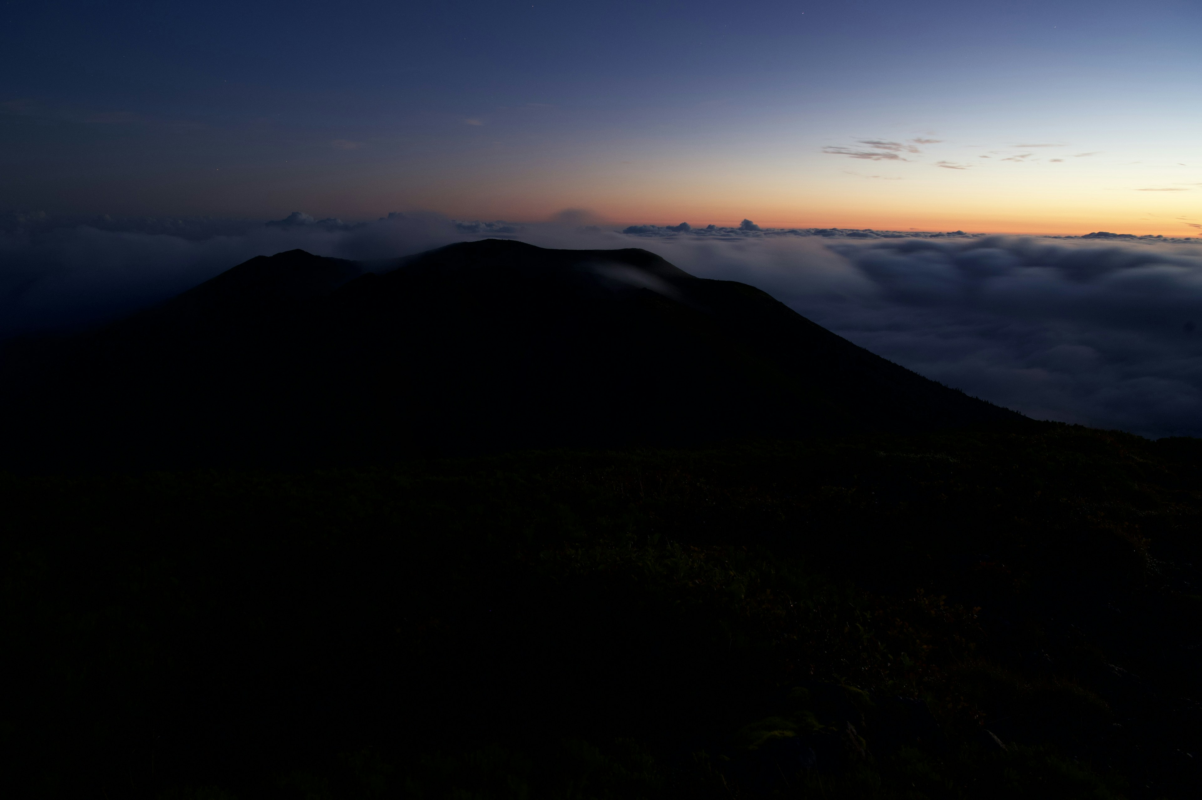 山のシルエットが雲の上に浮かび上がる夕暮れの風景