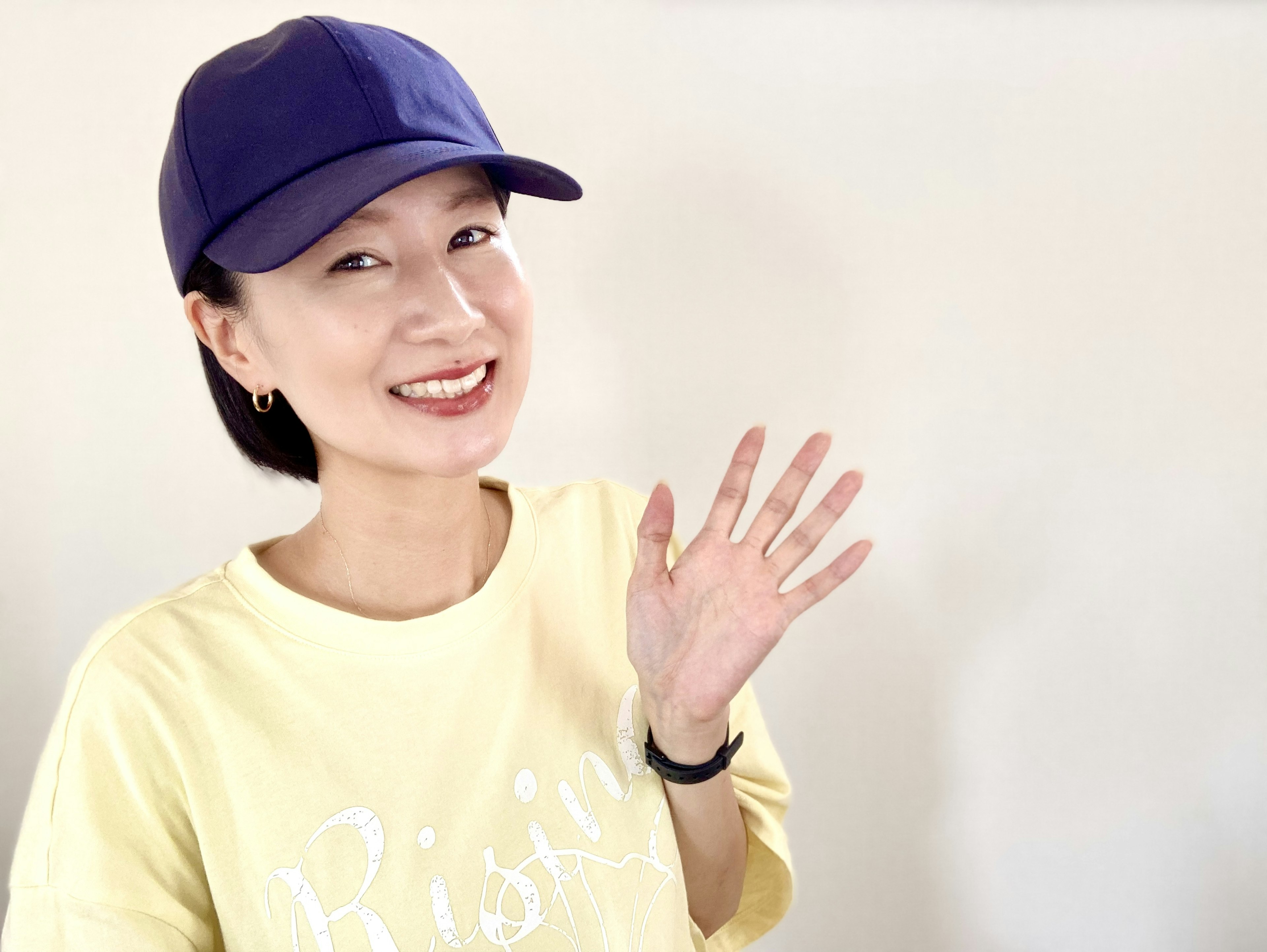 Smiling woman wearing a purple cap and yellow t-shirt waving her hand