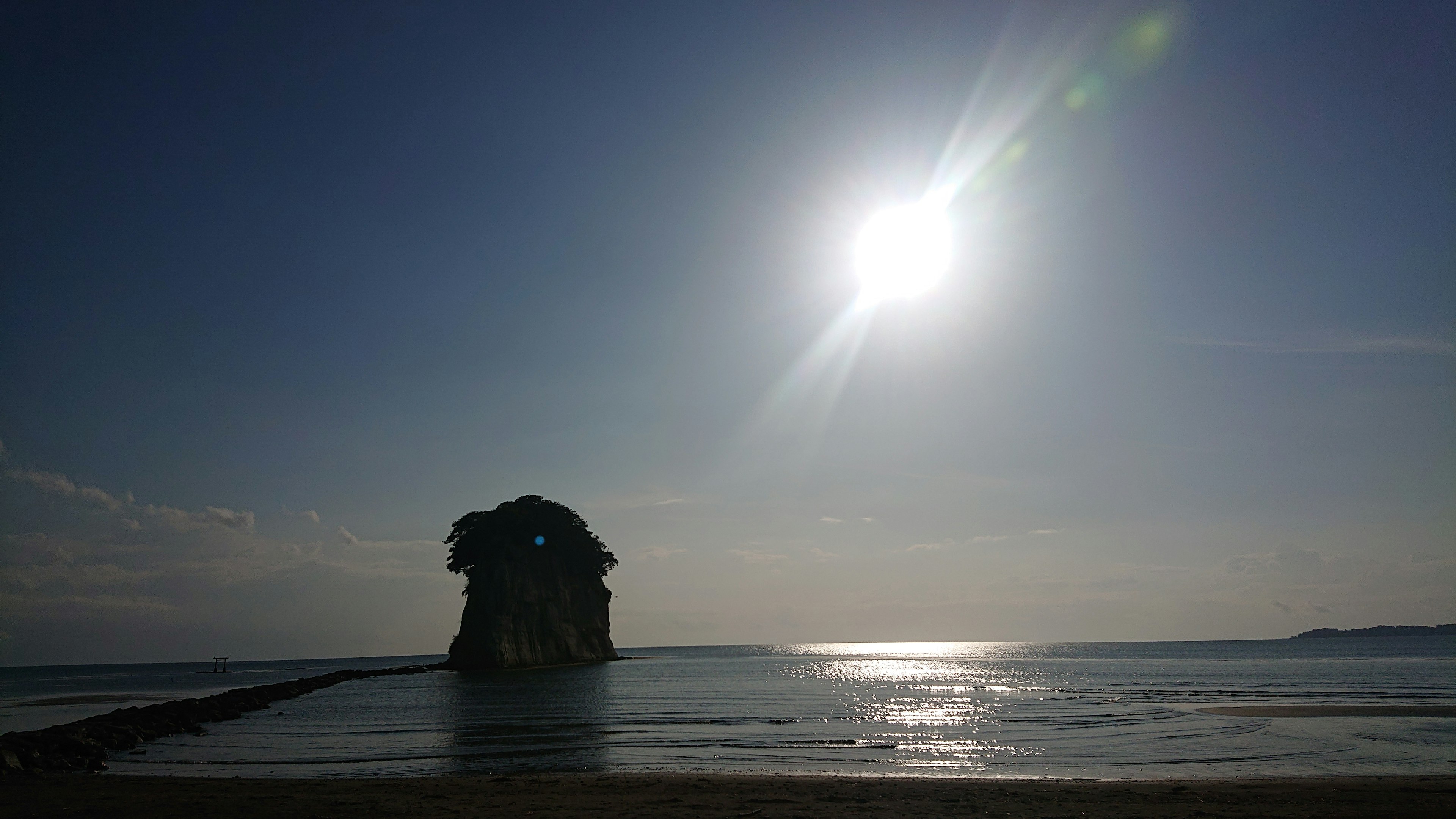 Un grande roccia nell'oceano con la luce del sole che si riflette su acque calme