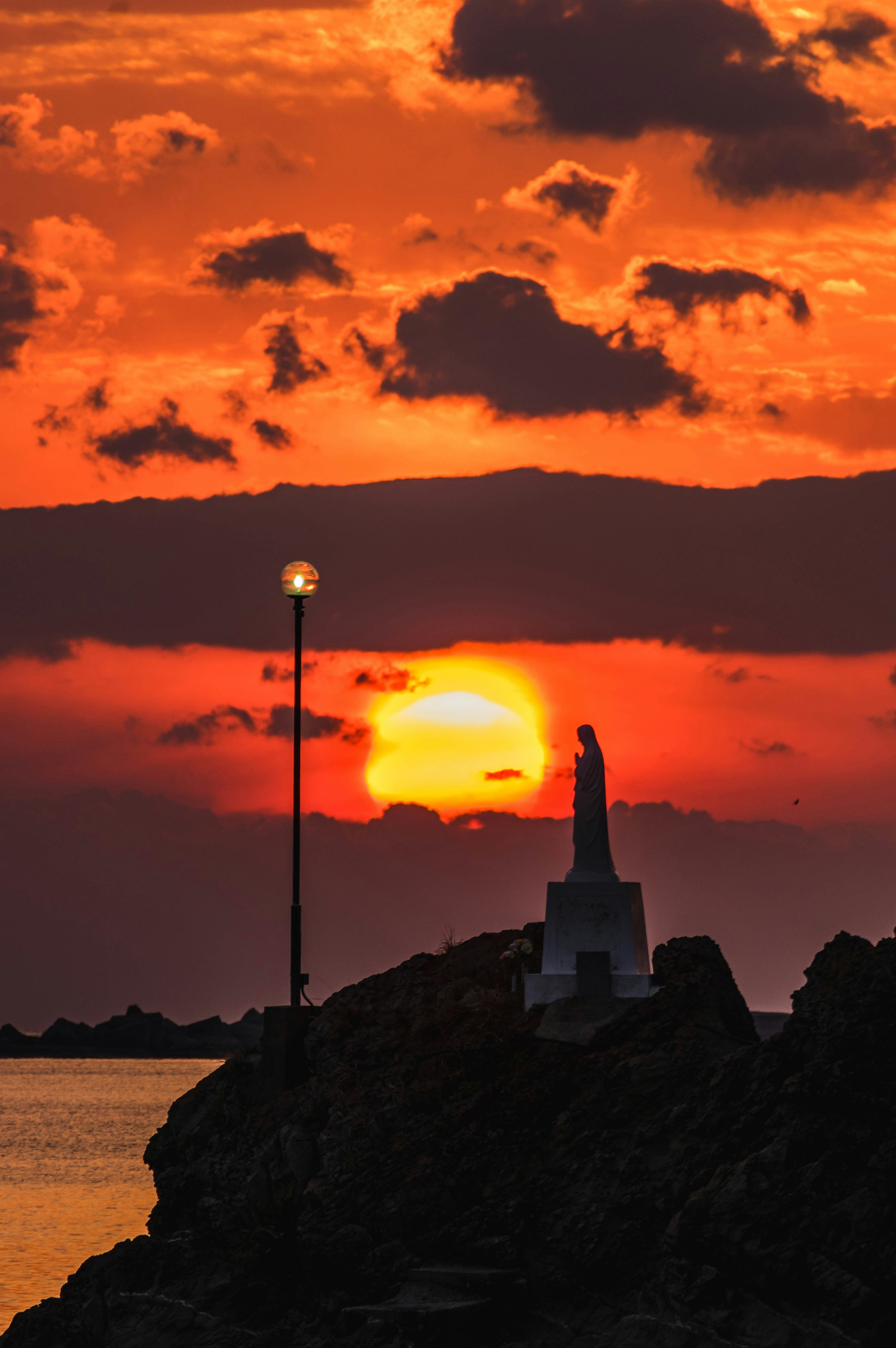 Silhouette einer Statue und eines Leuchtturms vor einem Sonnenuntergang