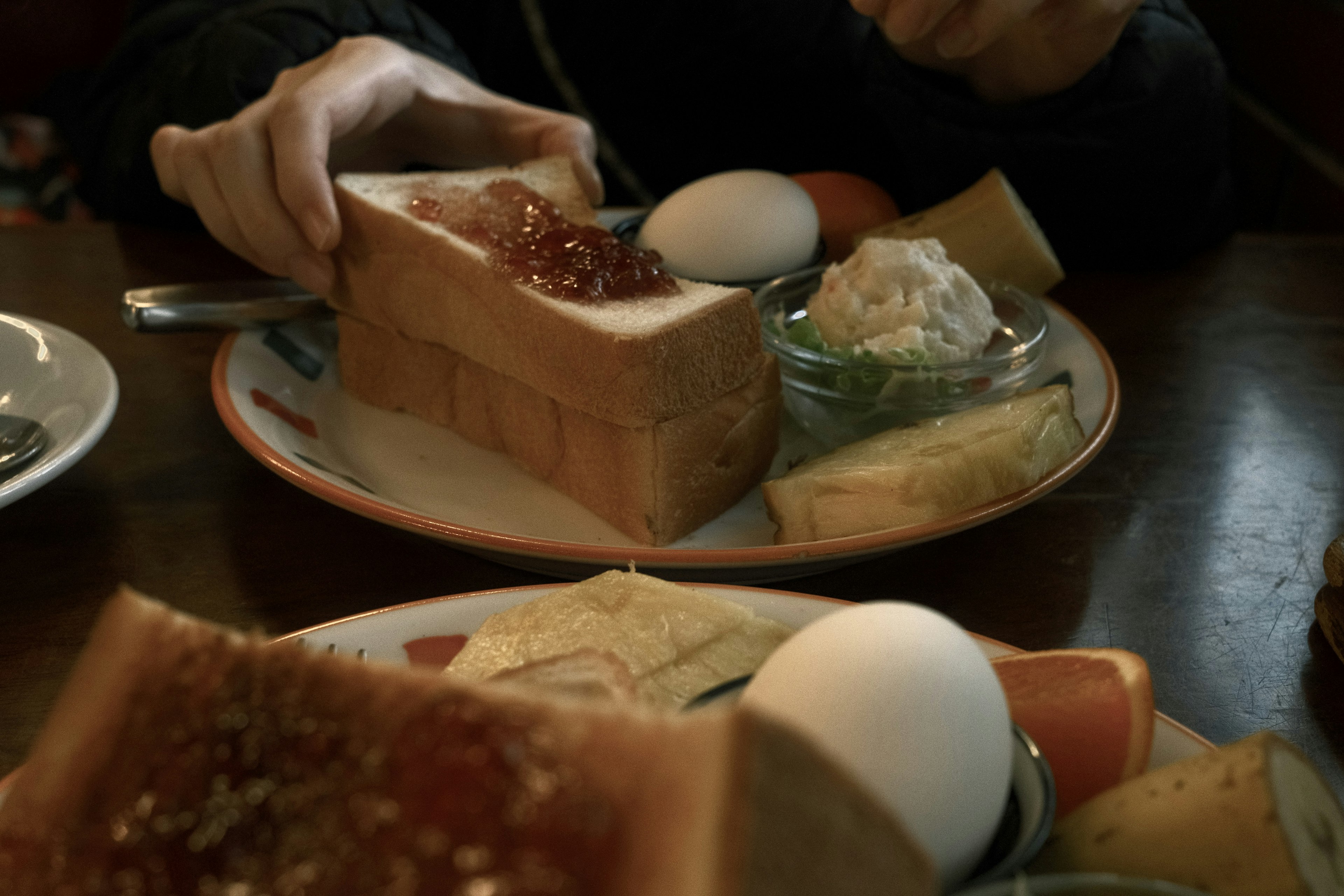 Breakfast scene featuring a hand holding toast with toppings and various side dishes