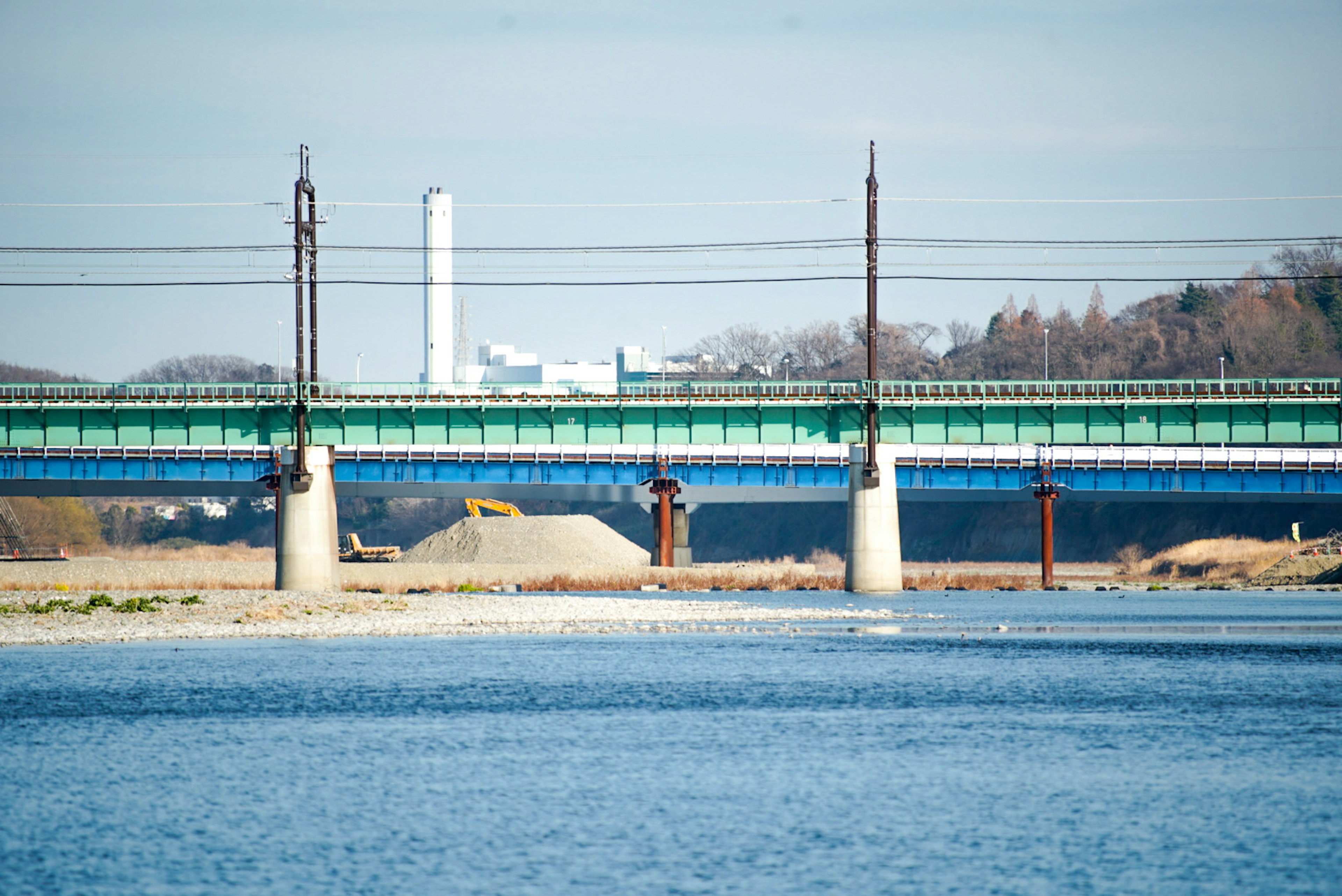 Grüne Eisenbahnbrücke über einen Fluss mit entferntem Fabrikschornstein