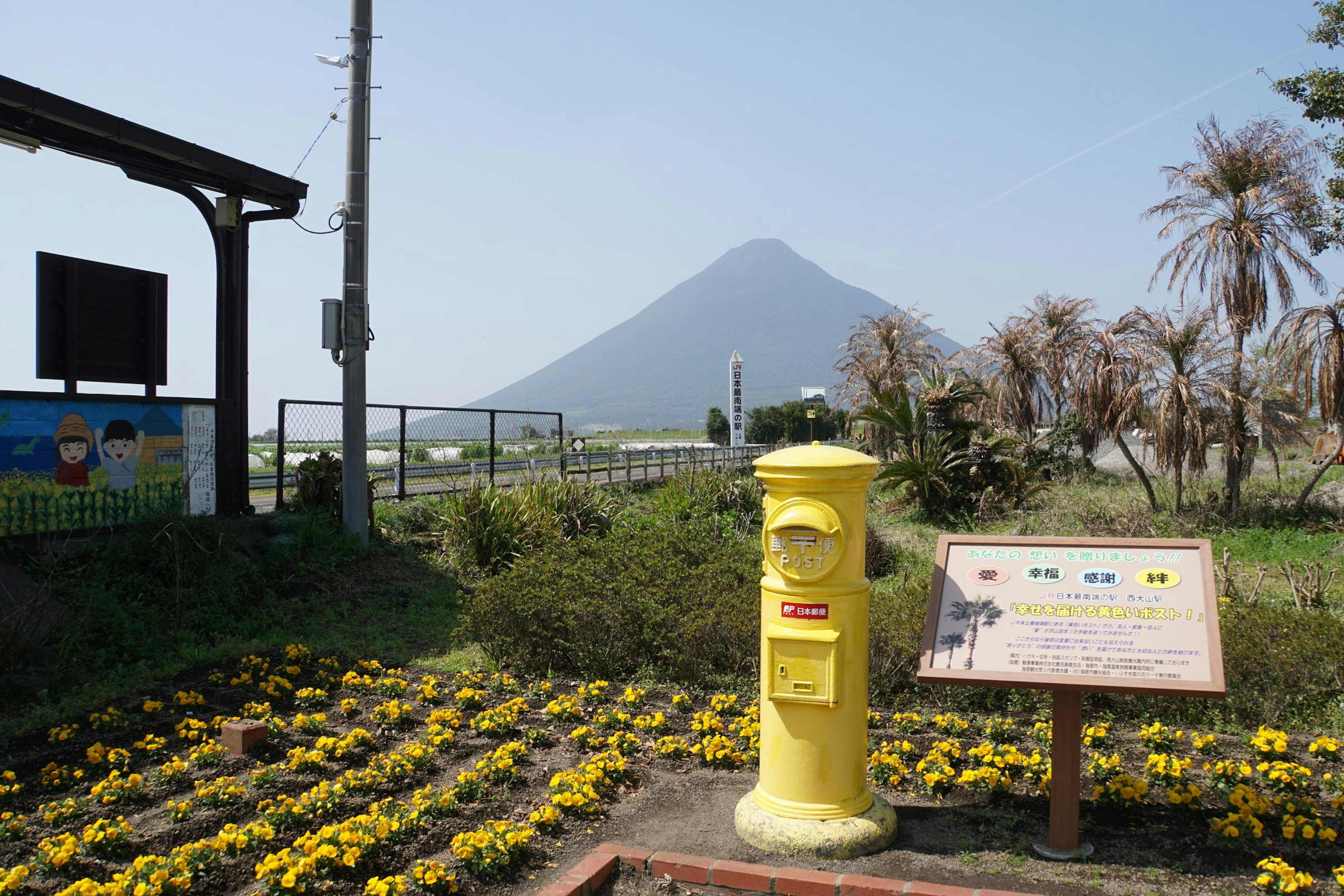 Boîte aux lettres jaune entourée de fleurs avec une montagne en arrière-plan