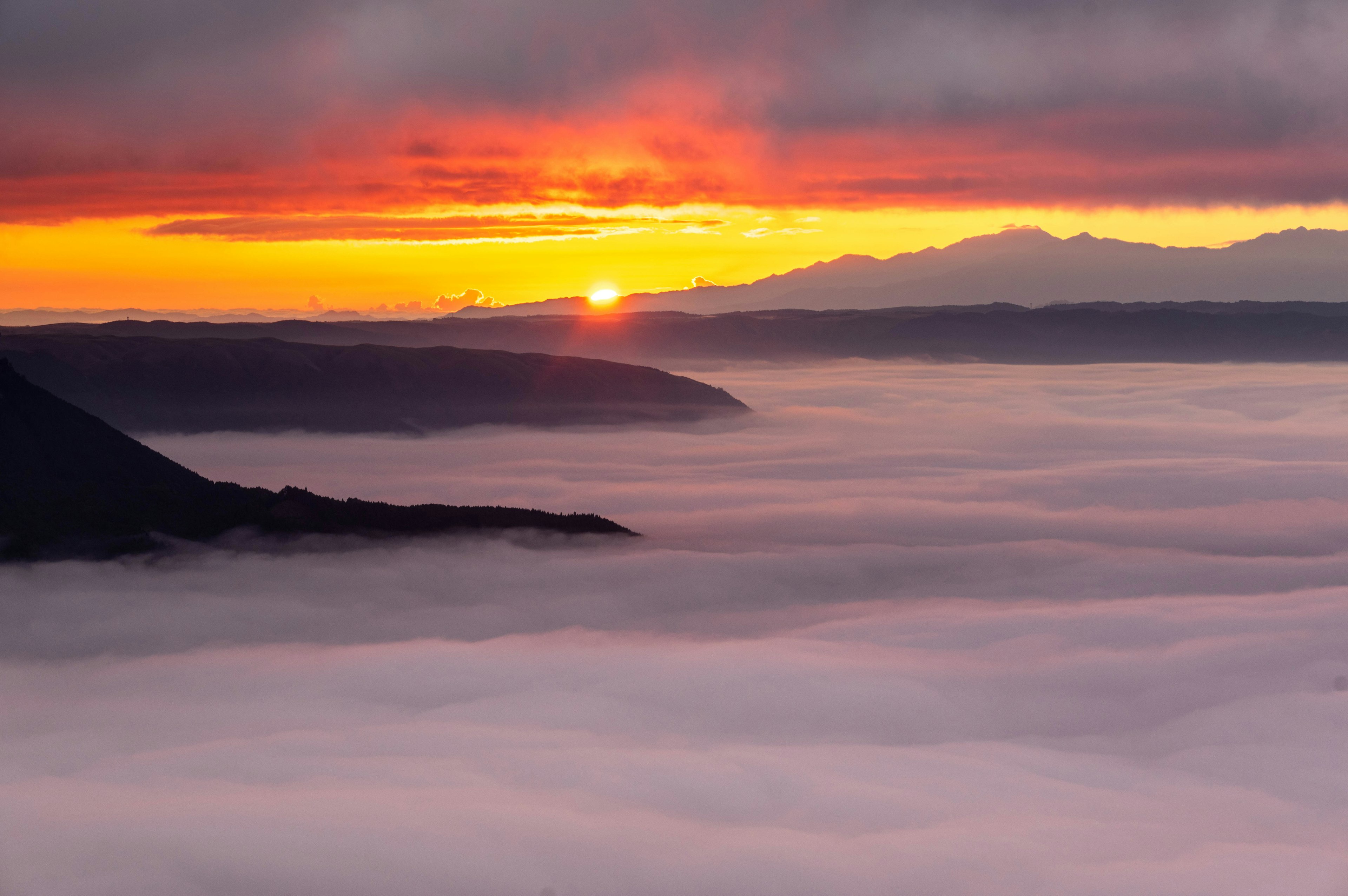 Wunderschöner Sonnenuntergang über einem Wolkenmeer mit Bergen im Hintergrund