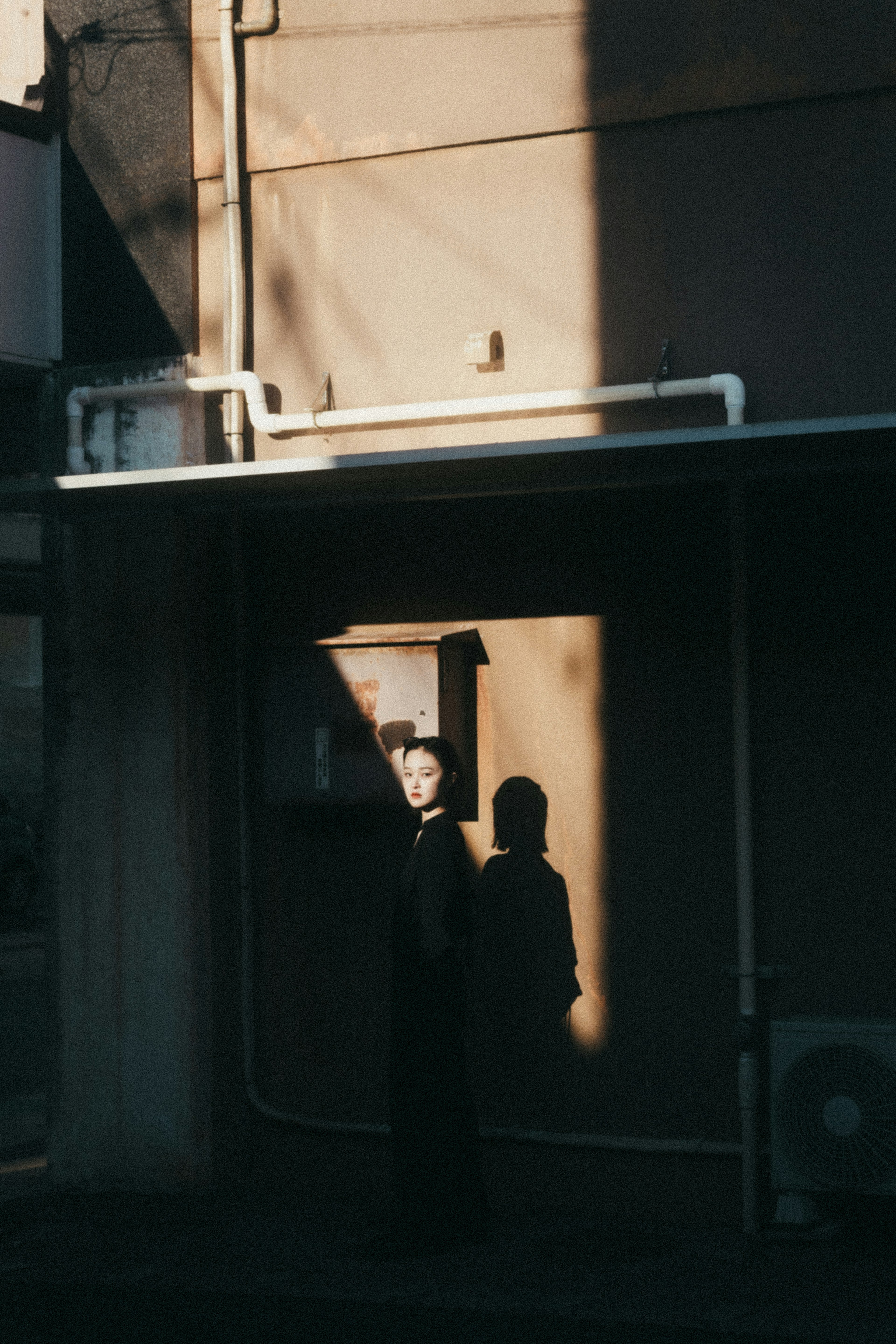 Silhouette of a person standing in front of a wall with shadows and building background