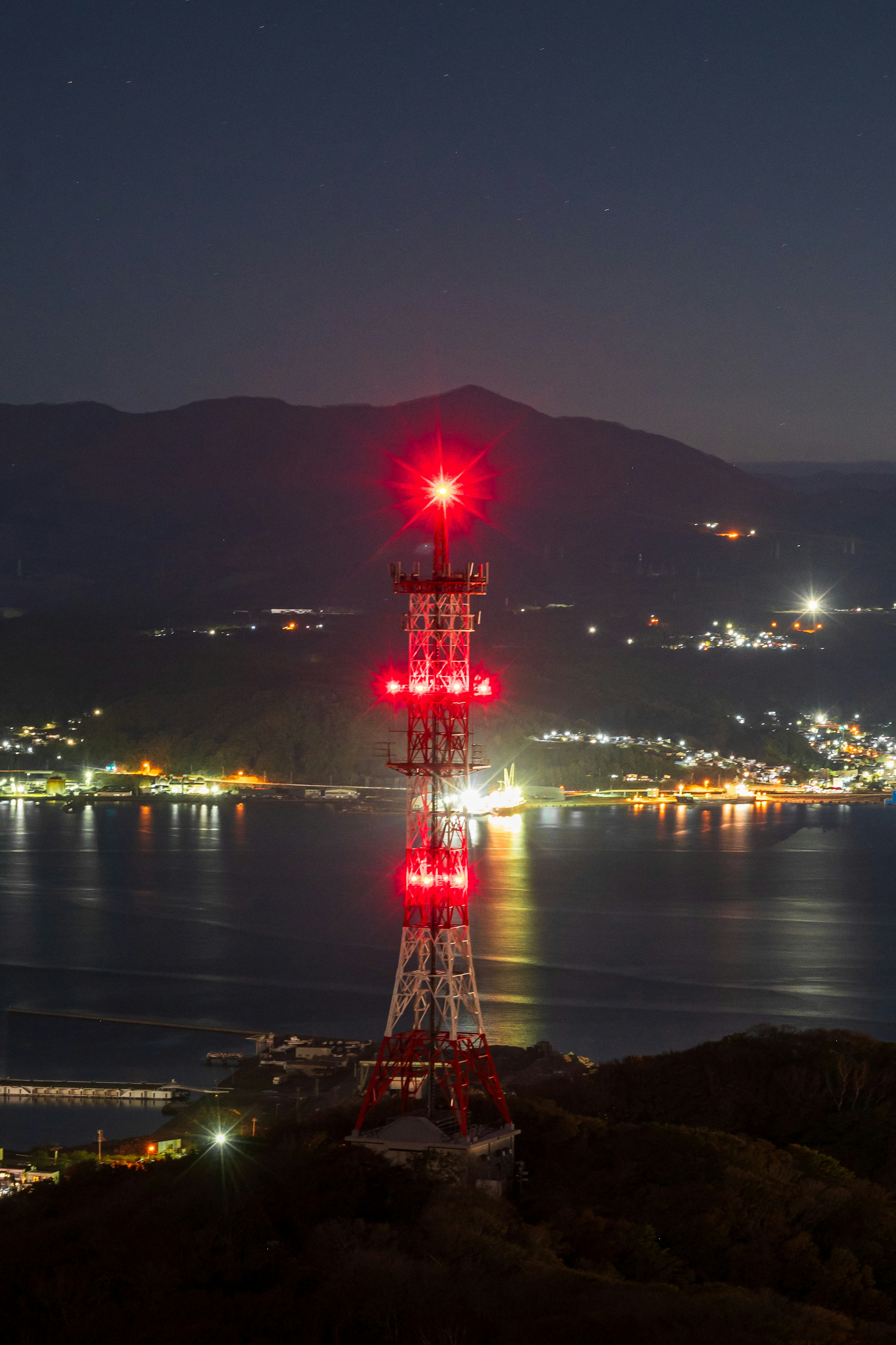 夜の海と山を背景にした赤い灯りを点灯した通信塔