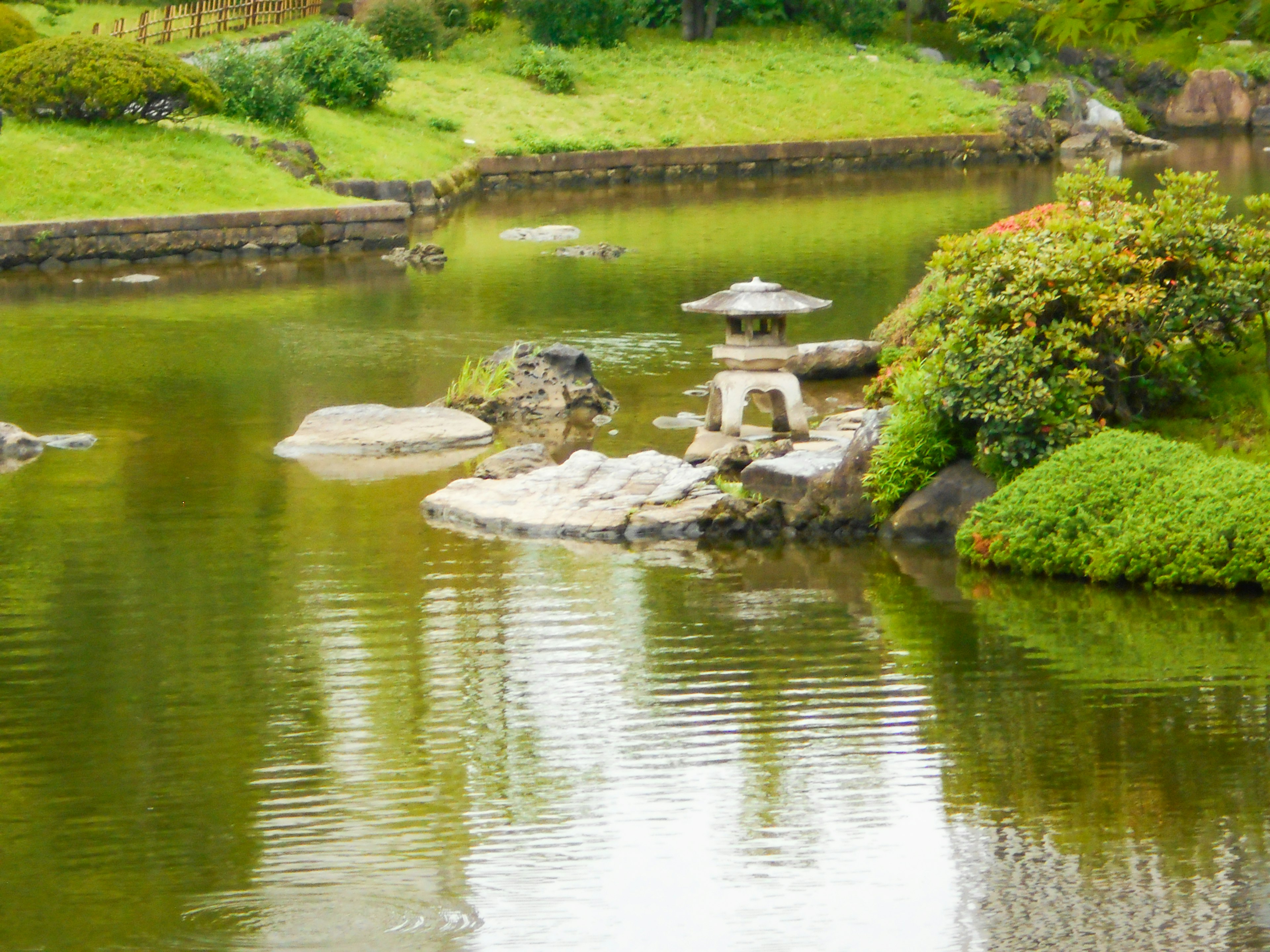 Stagno tranquillo di giardino giapponese con lanterna in pietra e vegetazione lussureggiante