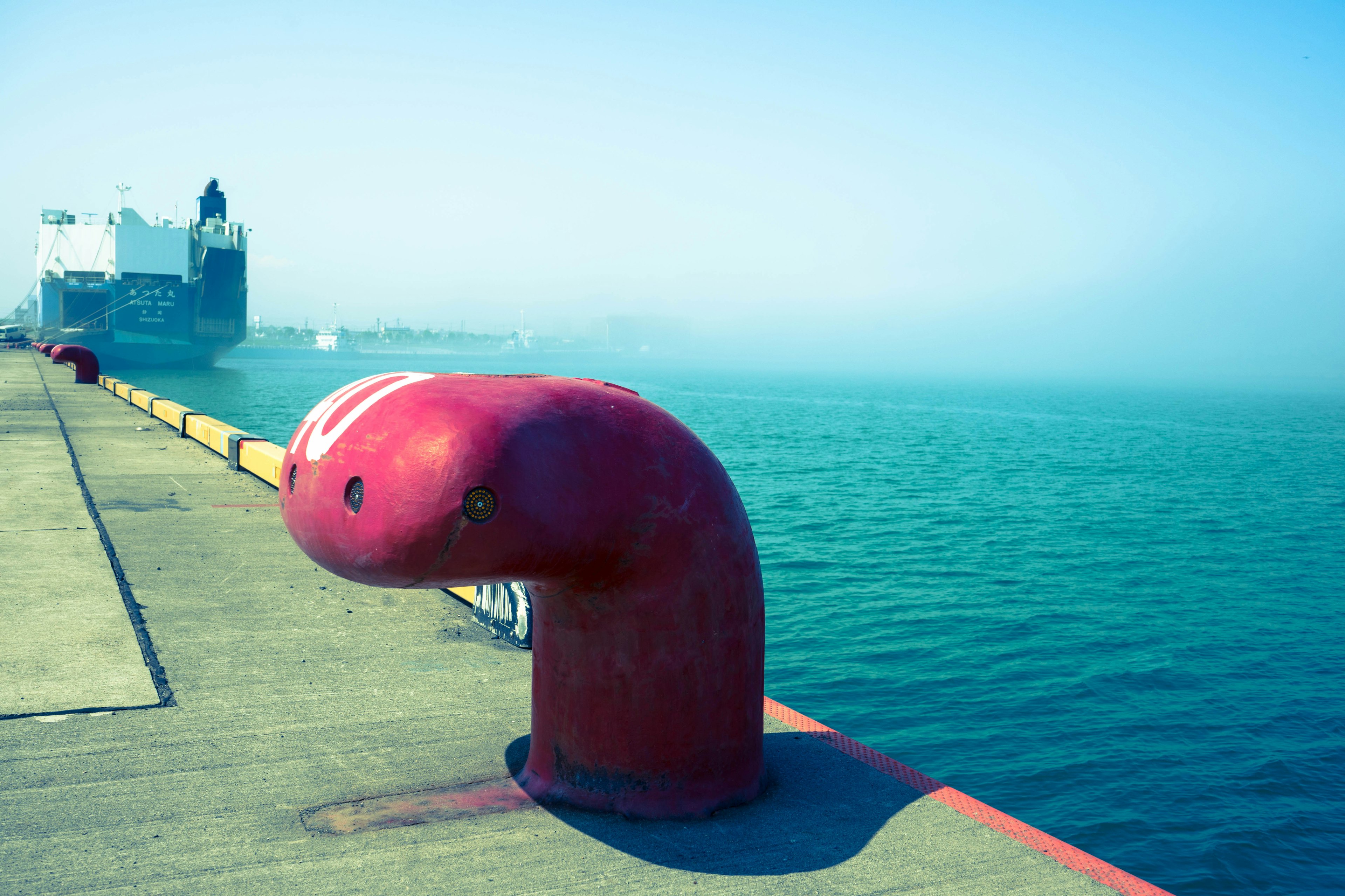 Bollard rouge sur un quai avec un navire flou en arrière-plan et une eau bleue calme