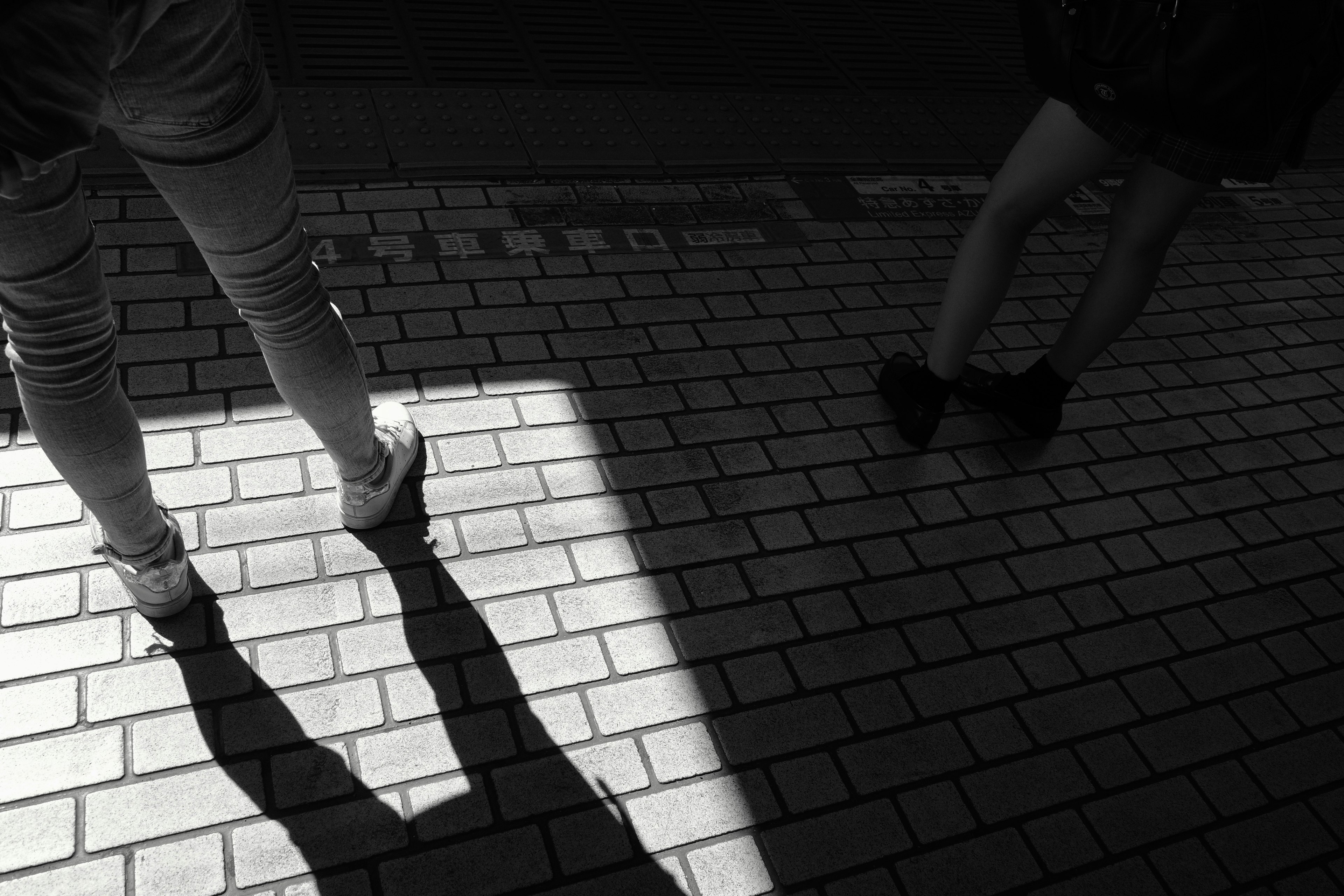 Two people standing on a paved street with shadows in black and white