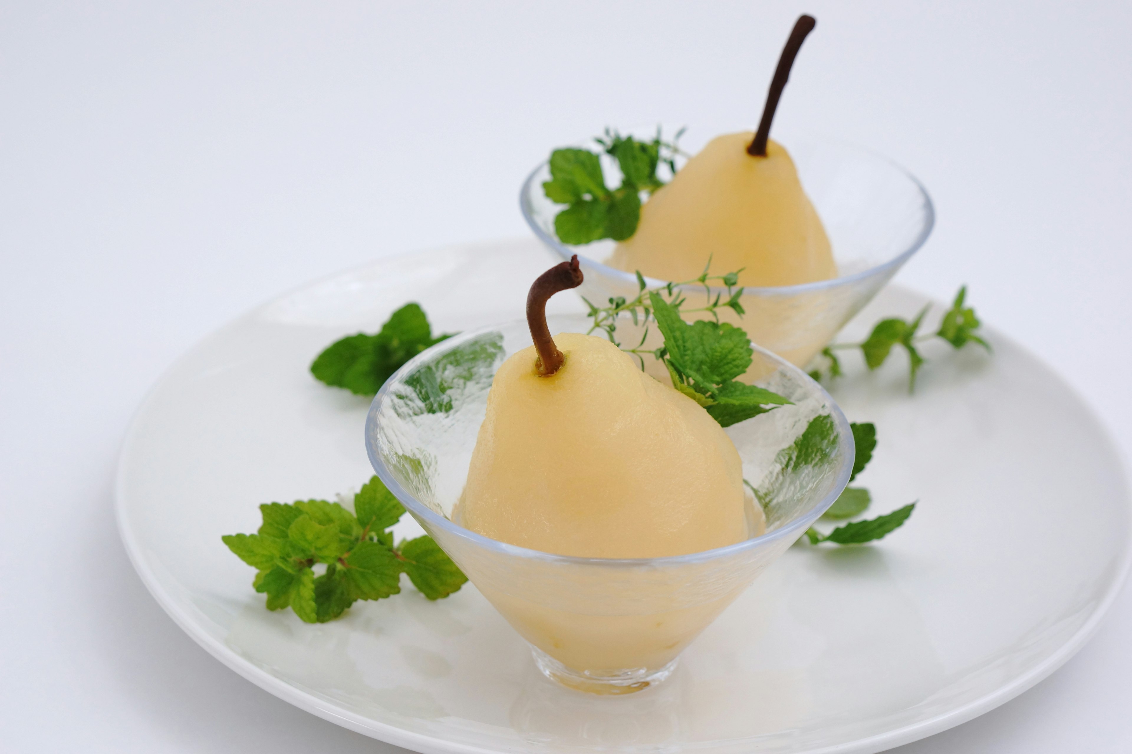 Two poached pears in transparent bowls garnished with mint leaves