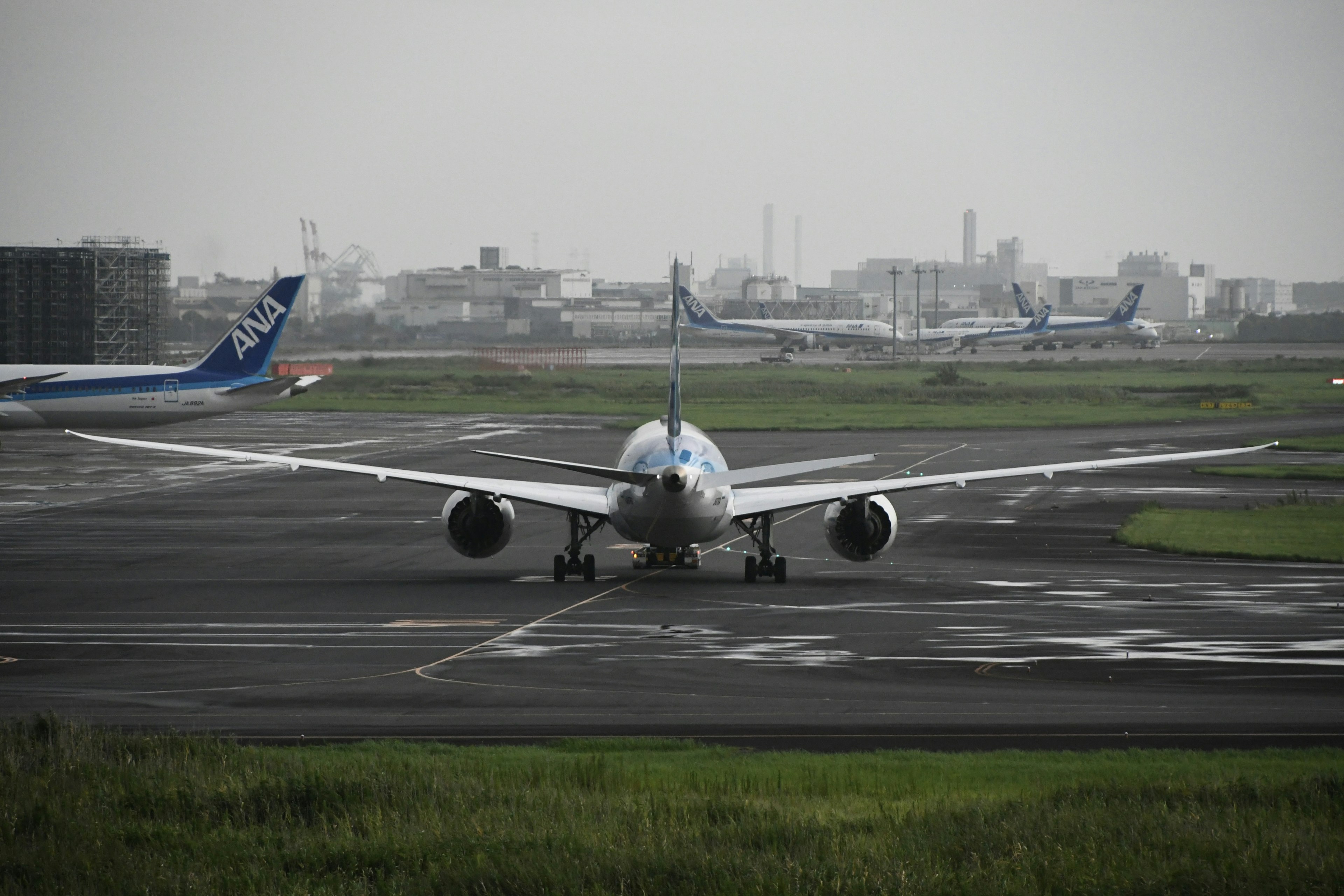 滑走路で待機する旅客機の後ろ姿と遠くに見える他の航空機