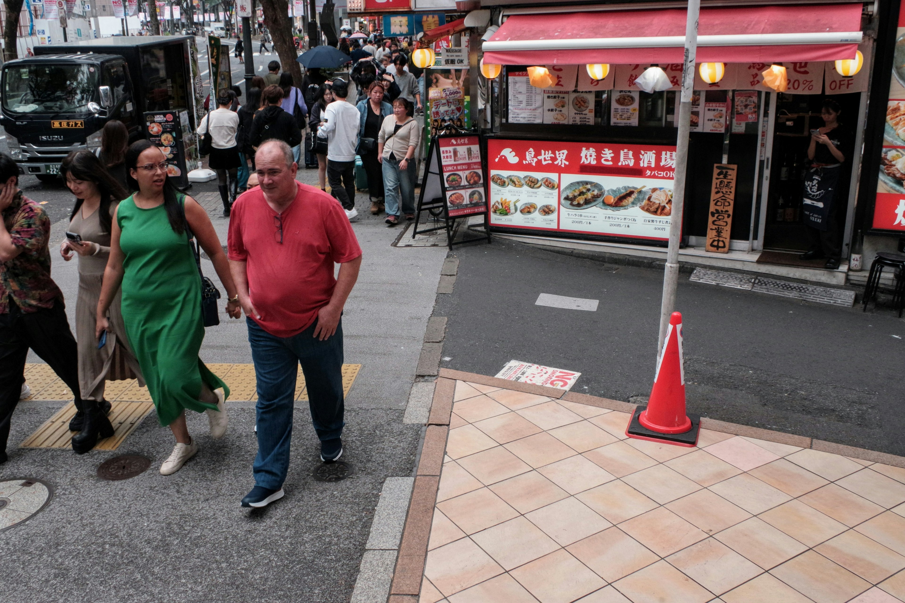 緑のドレスを着た女性と赤いシャツの男性が歩いている繁華街の風景