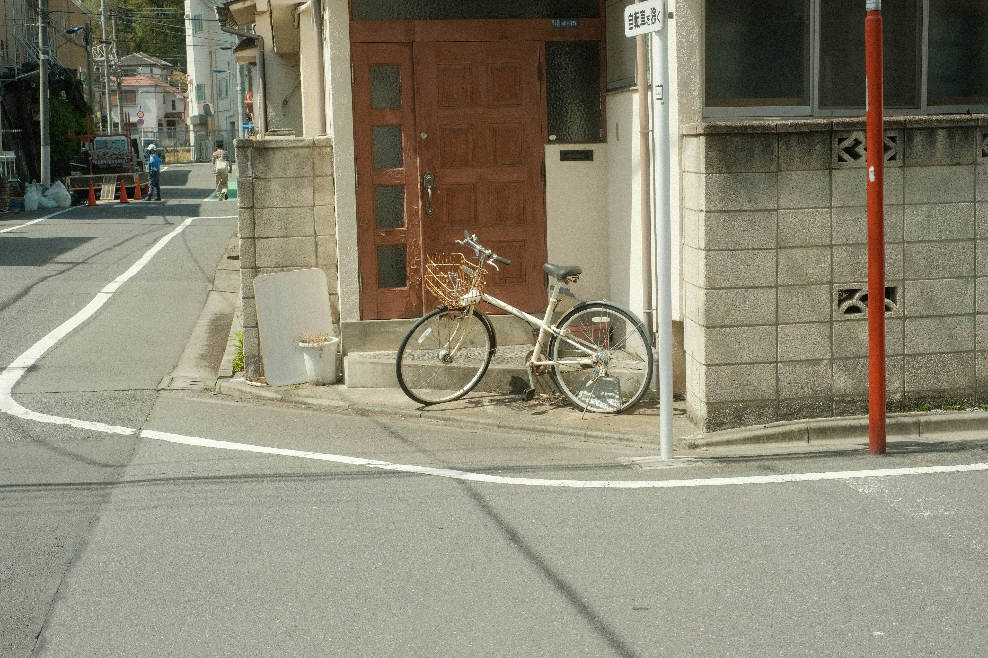 A white bicycle leaning against a wall near a wooden door in a street corner