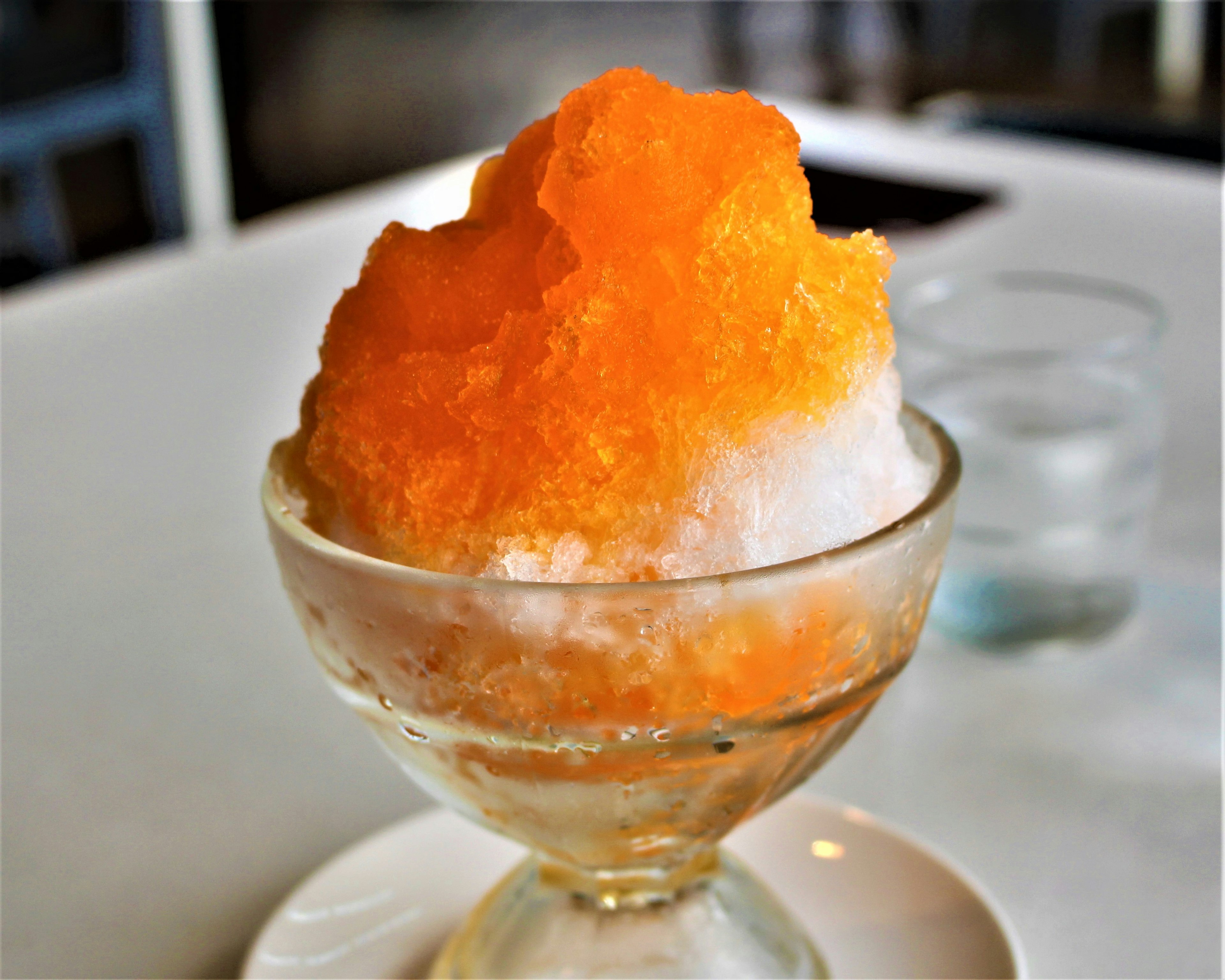 Un cono de nieve naranja brillante servido en un bol de vidrio transparente